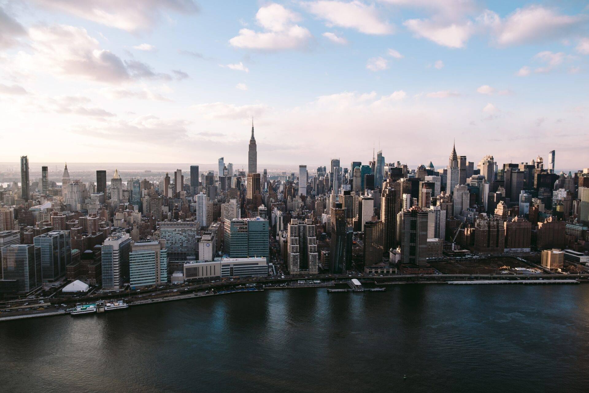 Vue aérienne d’une métropole américaine avec gratte-ciels iconiques, fleuve et waterfront sous un ciel dégagé