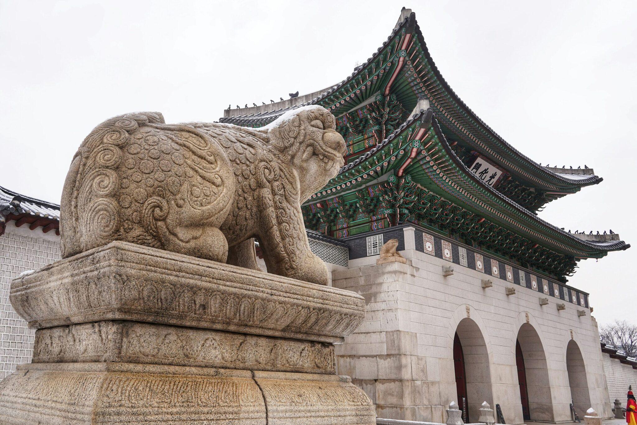 Une sculpture de lion en pierre devant un pavillon traditionnel coréen aux toits ornementés verts et rouges