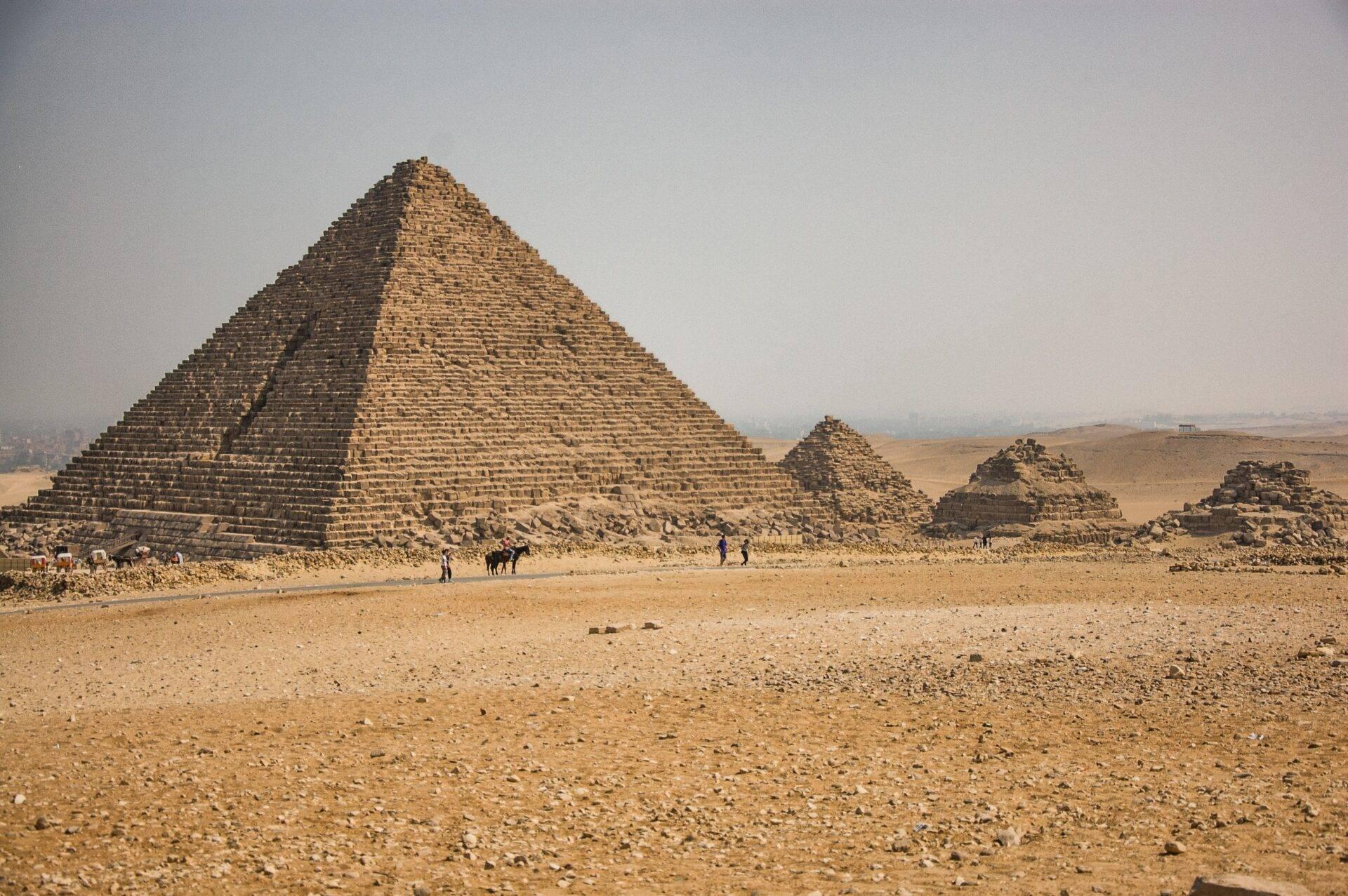 Une grande pyramide en pierre dans le désert égyptien avec des visiteurs et des ruines environnantes sous un ciel dégagé