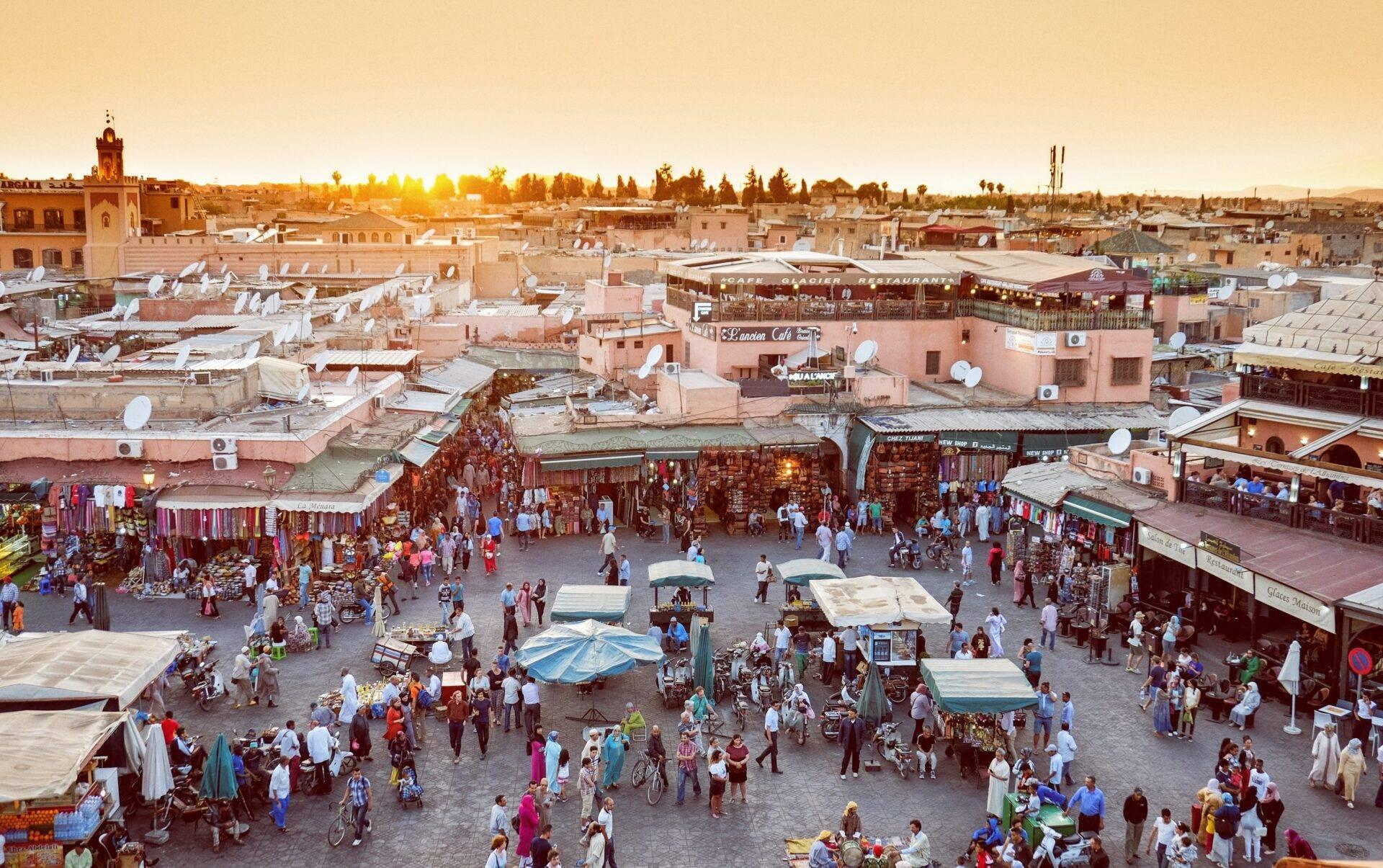Vue aérienne d’une médina marocaine animée avec marché, bâtiments ocre et foule de visiteurs au coucher du soleil