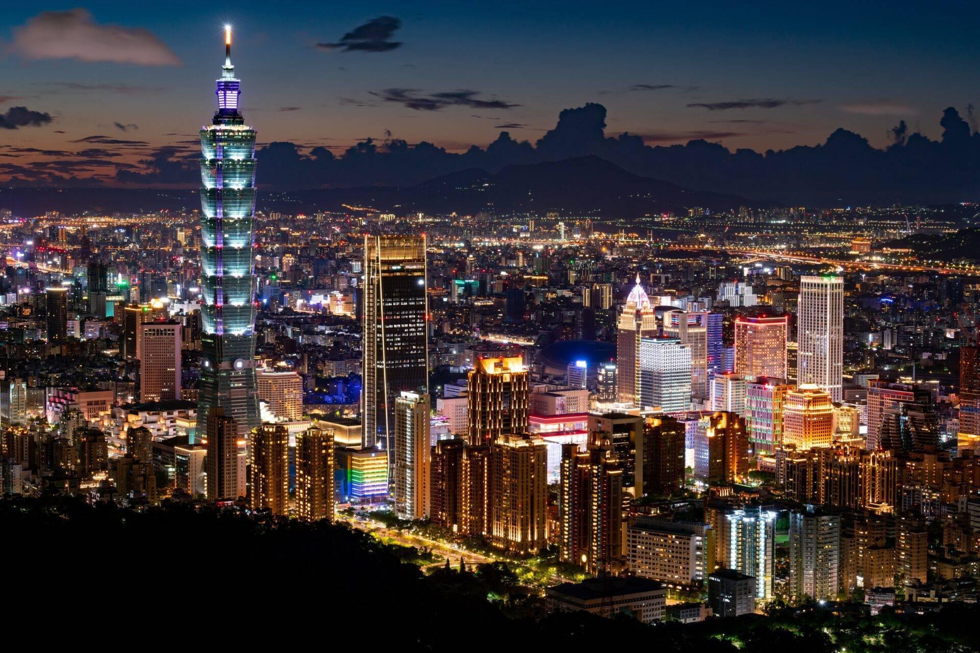 Vue nocturne d’une métropole asiatique illuminée avec une tour distinctive éclairée en bleu dominant le skyline urbain
