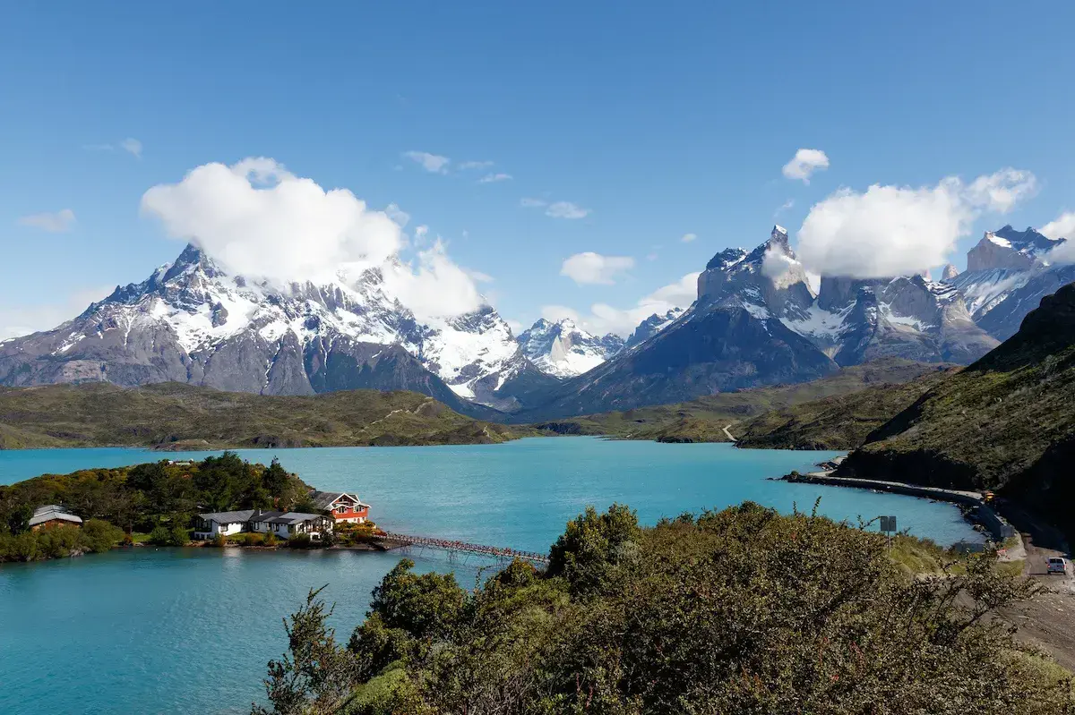 Lac turquoise entouré de montagnes enneigées avec lodge et végétation verte sous ciel dégagé