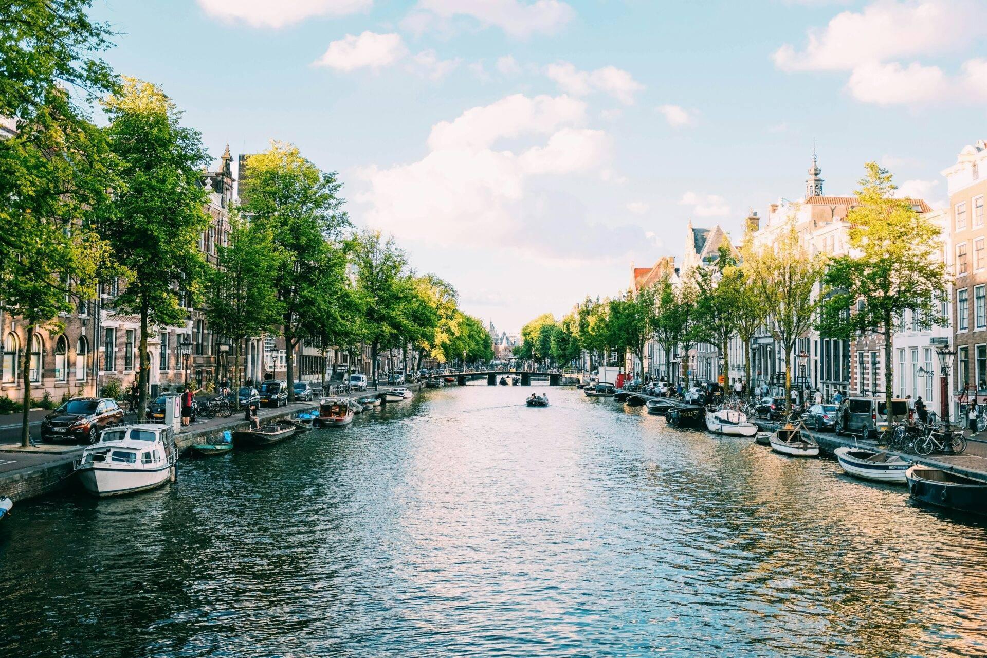 Un canal urbain bordé de maisons colorées, avec des bateaux amarrés et des arbres verts sous un ciel ensoleillé