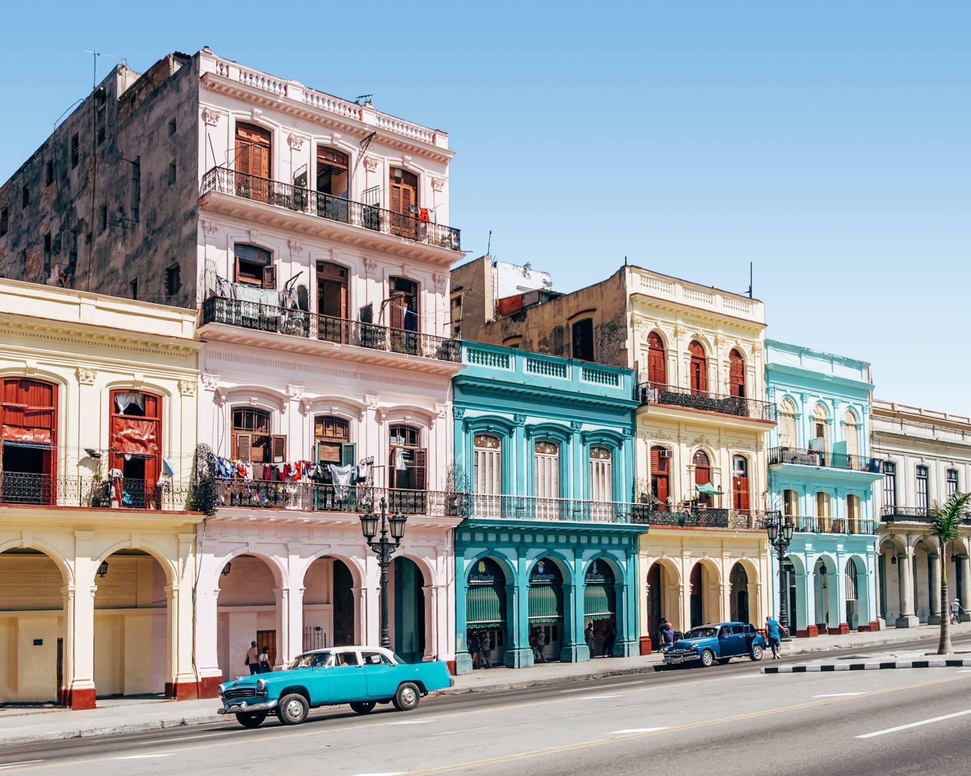 Une rue coloniale avec des bâtiments colorés aux façades pastel et une voiture vintage turquoise