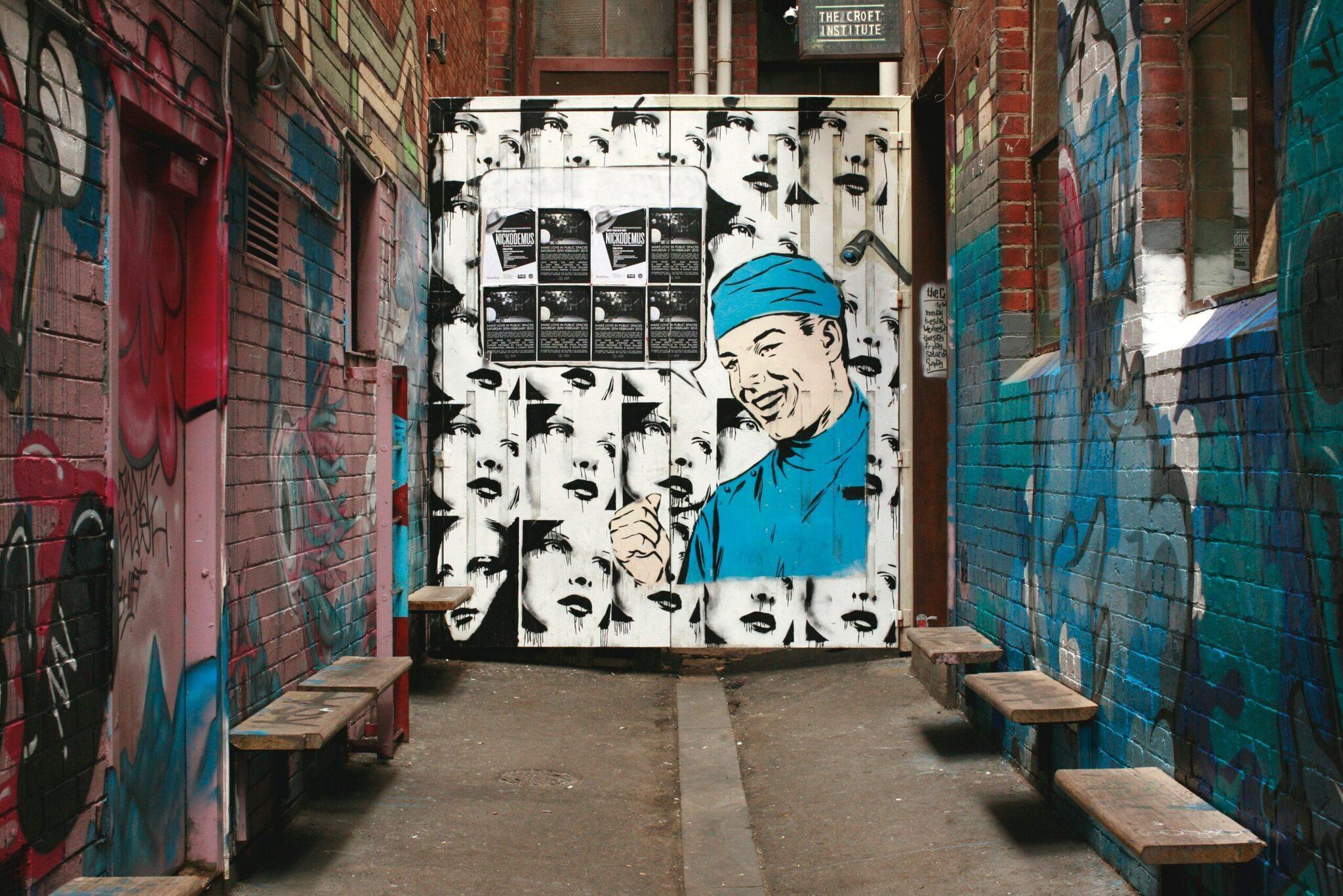 Une ruelle urbaine avec street art coloré montrant un personnage en bleu parmi des portraits en noir et blanc