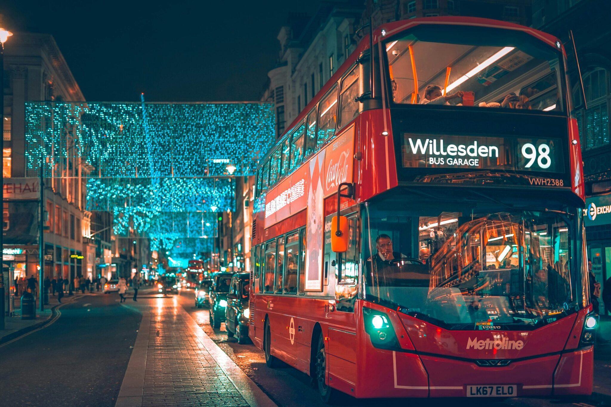 Un bus à impériale rouge circulant de nuit dans une rue londonienne illuminée de décorations bleues féeriques