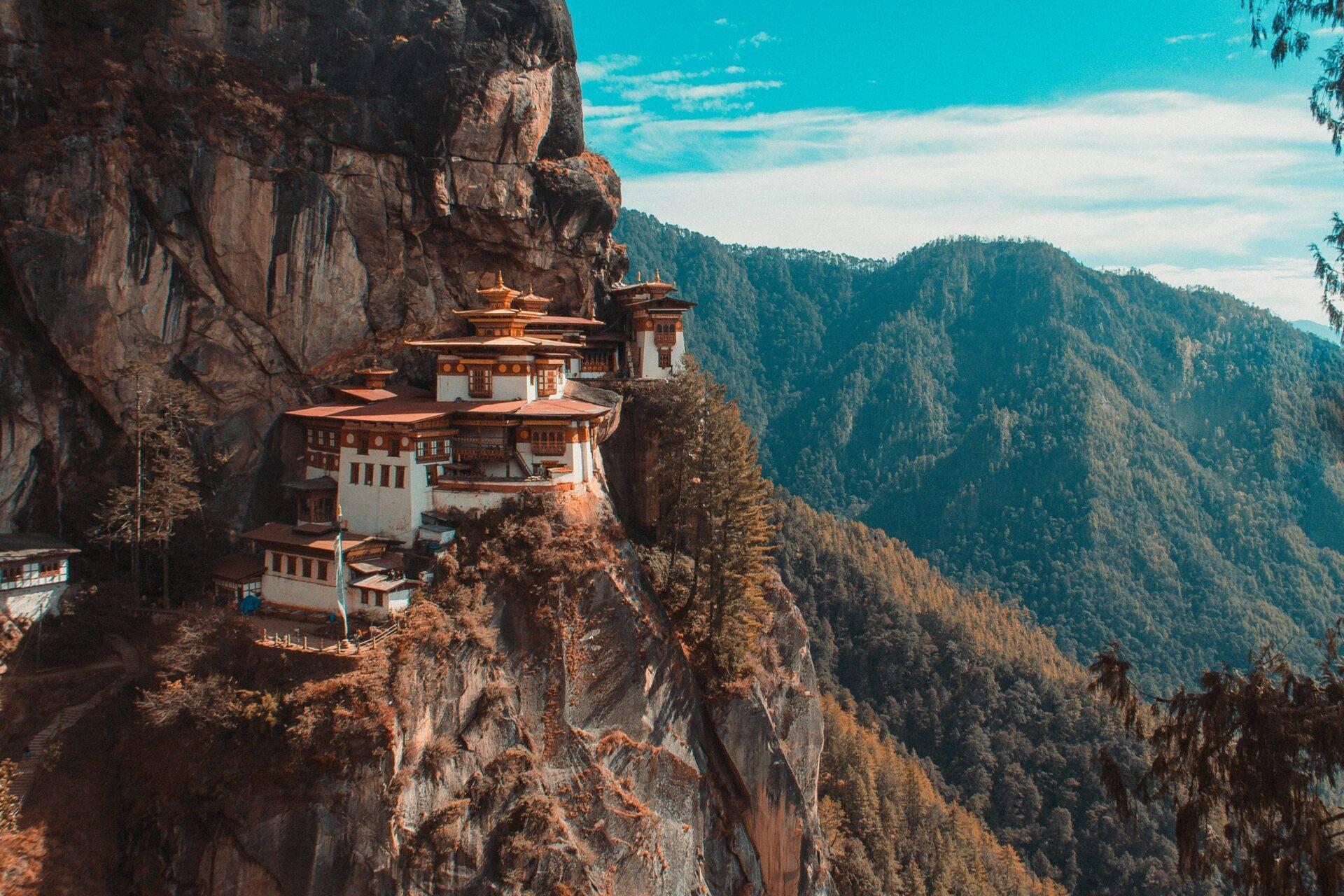 Un monastère aux toits rouges et blancs perché sur une falaise rocheuse entourée de montagnes boisées verdoyantes