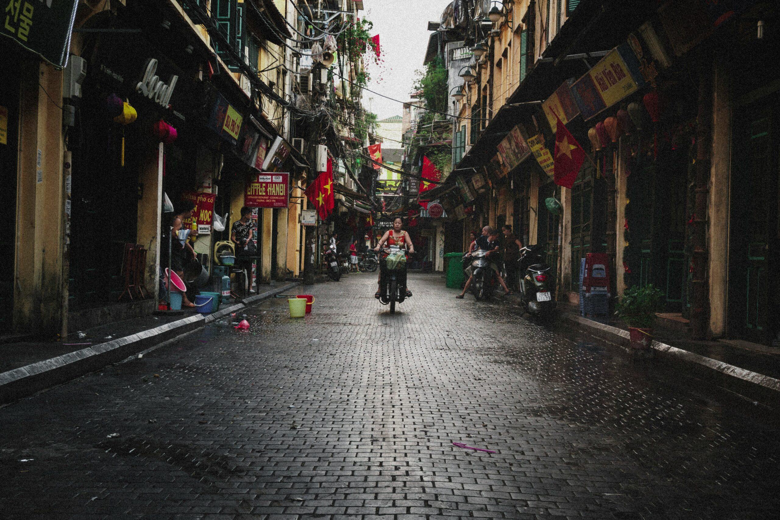 Une ruelle étroite du Vieux Quartier avec façades jaunes, drapeaux rouges et motos, ambiance authentique urbaine asiatique