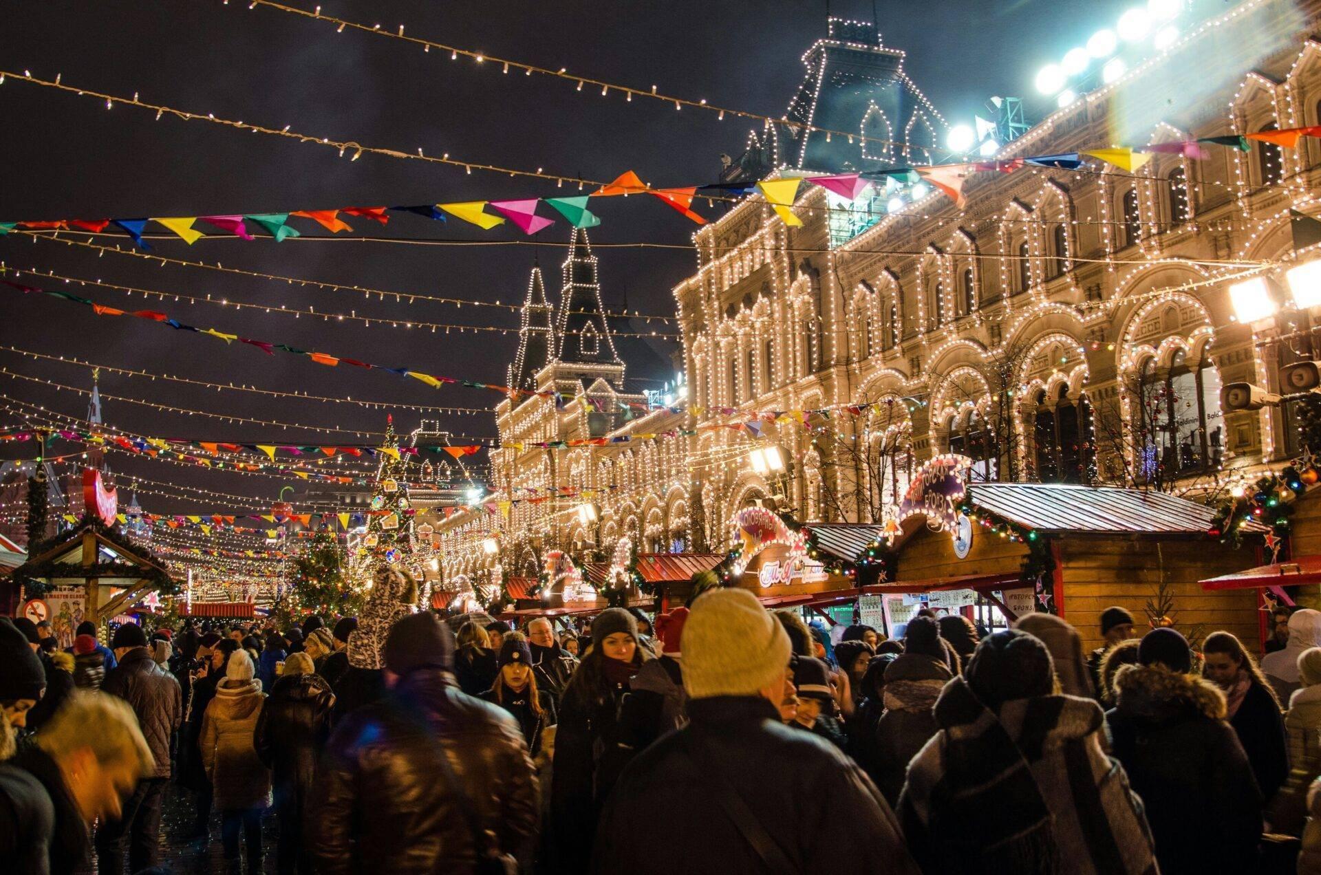 Marché de Noël nocturne illuminé avec bâtiments historiques décorés, foule festive et guirlandes colorées
