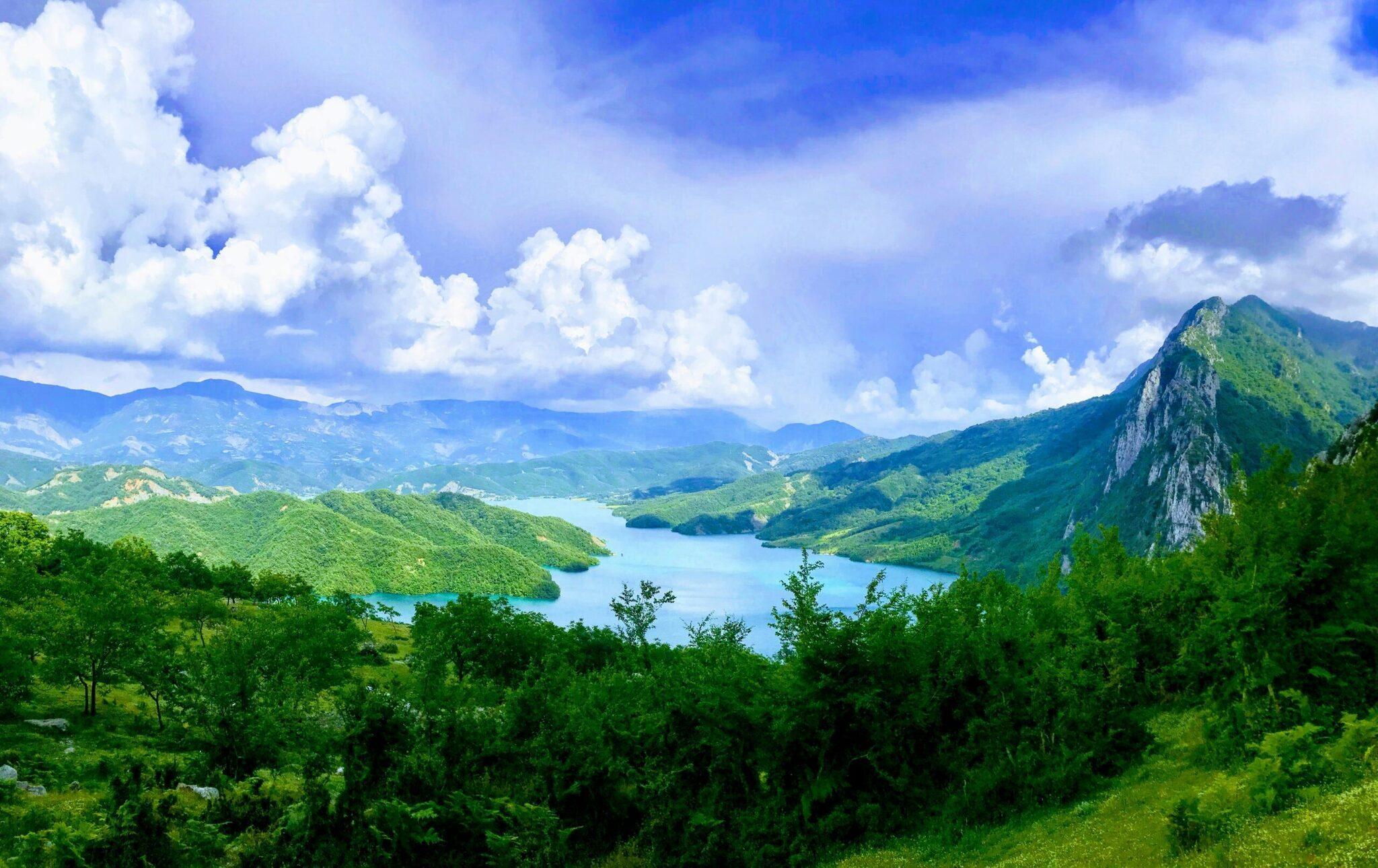 Vue panoramique d’un lac alpin turquoise entouré de montagnes verdoyantes et d’une falaise rocheuse imposante