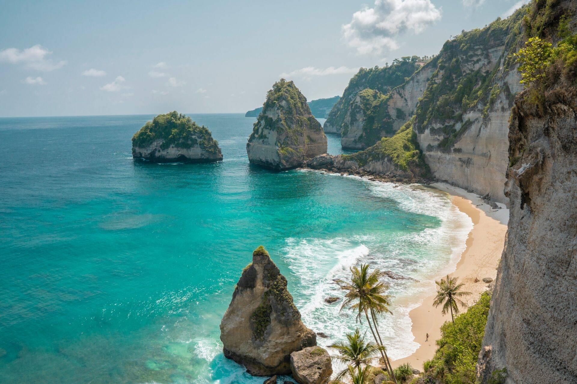 Plage tropicale avec falaises calcaires blanches, îlots rocheux et eaux turquoise cristallines bordées de palmiers