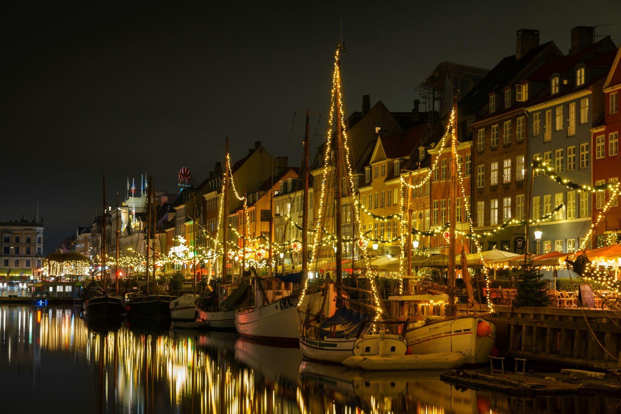 Un port historique illuminé de guirlandes dorées la nuit avec des bateaux traditionnels et bâtiments colorés