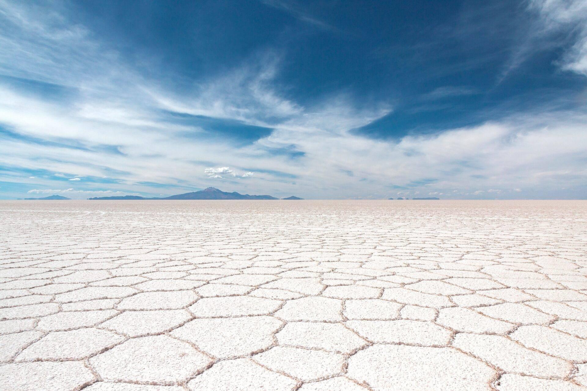 Vaste plaine de sel blanc craquelée avec montagnes lointaines sous ciel bleu nuageux