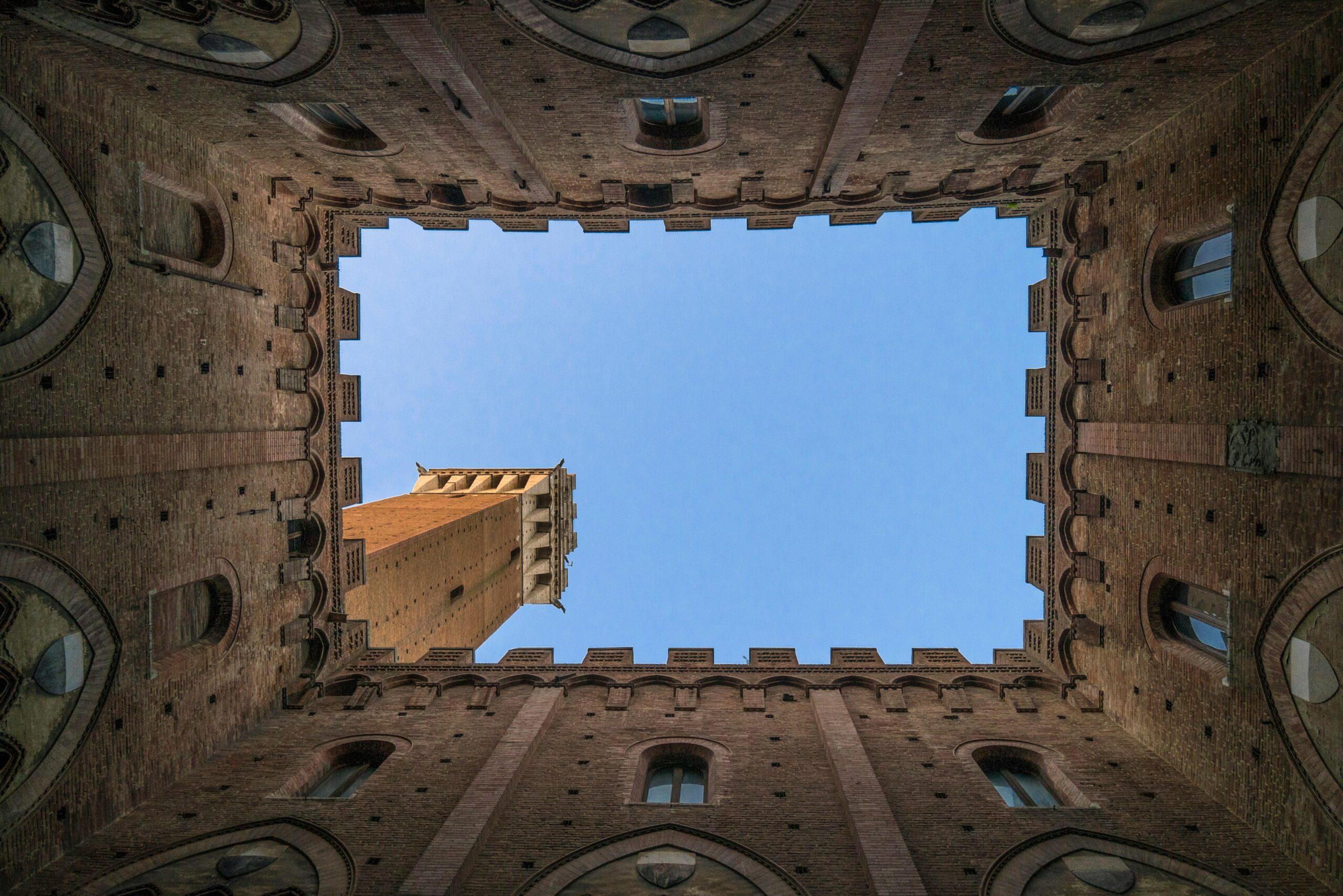 Vue en contre-plongée d’une cour intérieure de palais médiéval italien en brique avec ciel bleu