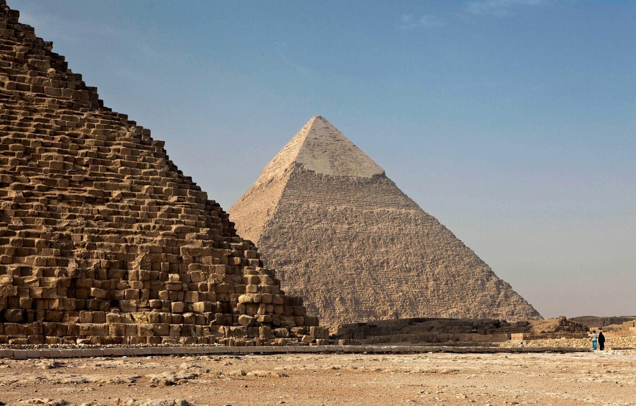Deux pyramides en pierre calcaire dans le désert égyptien sous un ciel dégagé, avec des visiteurs au premier plan