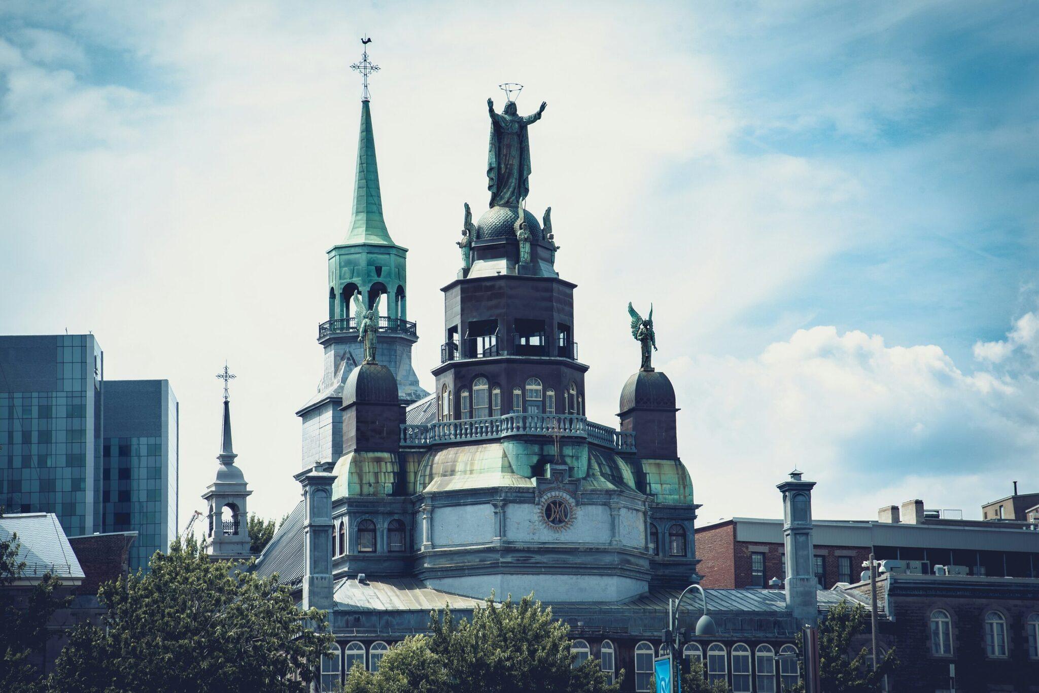 Cathédrale avec dôme de cuivre turquoise et statue angélique dominant le skyline urbain sous ciel bleu nuageux