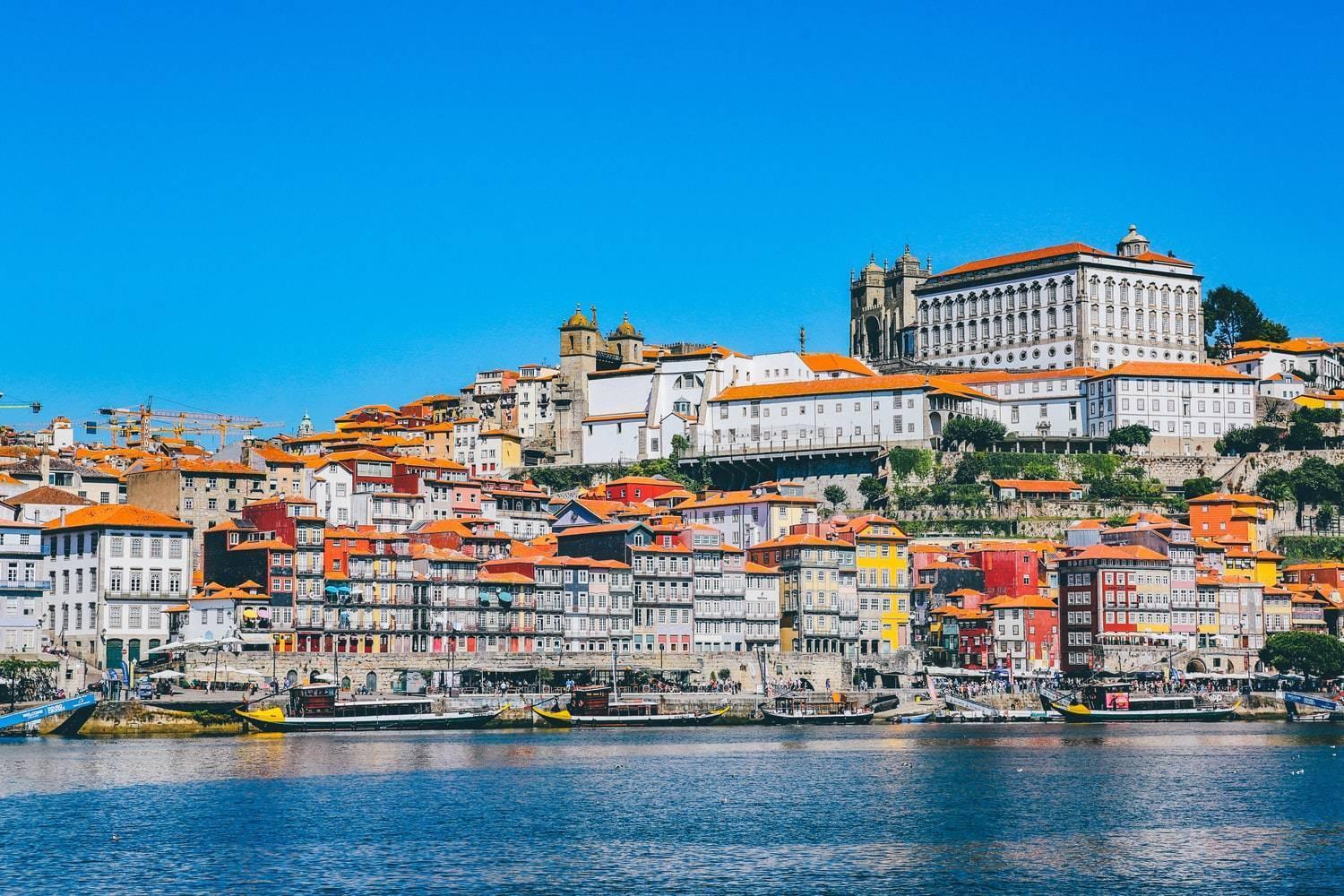 Vue panoramique d’une ville portuaire avec maisons colorées aux toits orangés dominant le fleuve sous ciel bleu