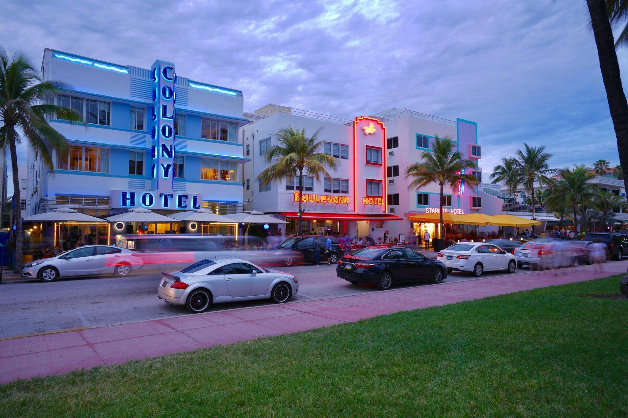 Hôtels Art Déco illuminés au crépuscule avec voitures garées sur une avenue tropicale