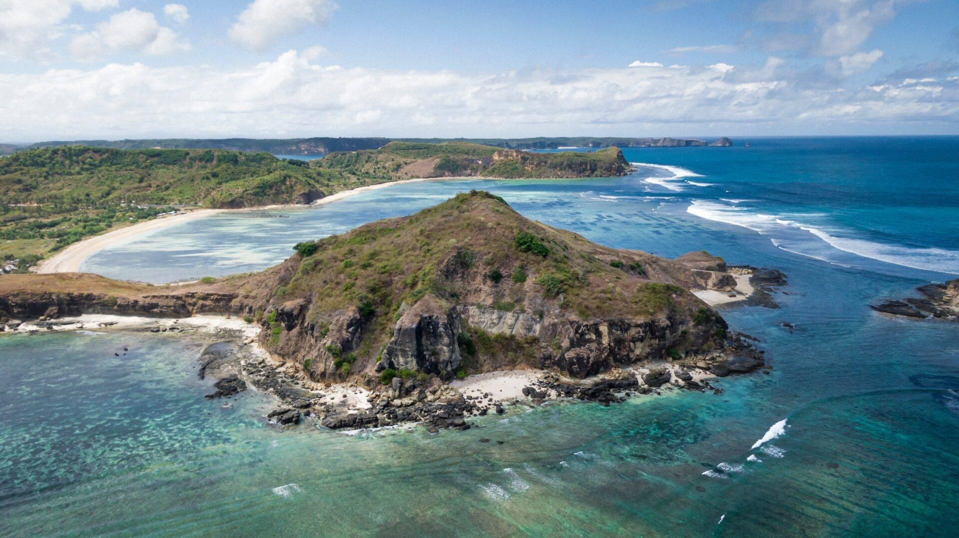 Vue aérienne d’une péninsule rocheuse entourée d’eaux turquoise avec plage de sable blanc et côtes verdoyantes
