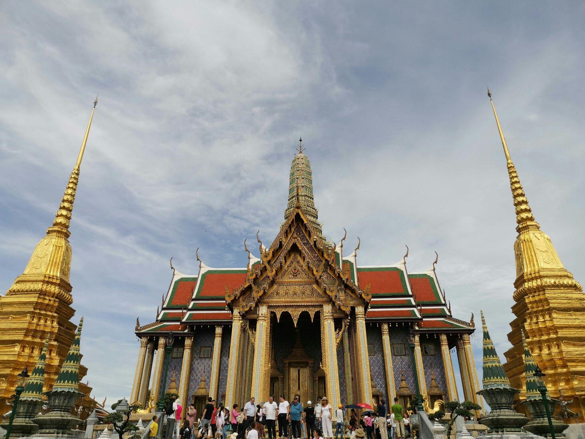 Un temple thaïlandais aux toits rouges et ornements dorés avec des visiteurs sur la grande esplanade
