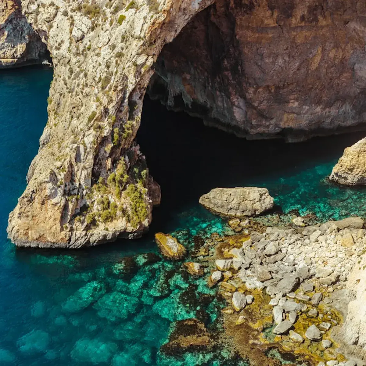 Grotte côtière calcaire surplombant une eau turquoise cristalline et des roches colorées