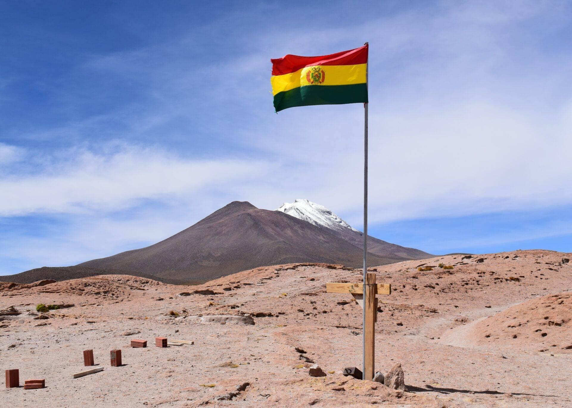 Le drapeau bolivien flotte dans un désert aride face à un volcan enneigé en arrière-plan