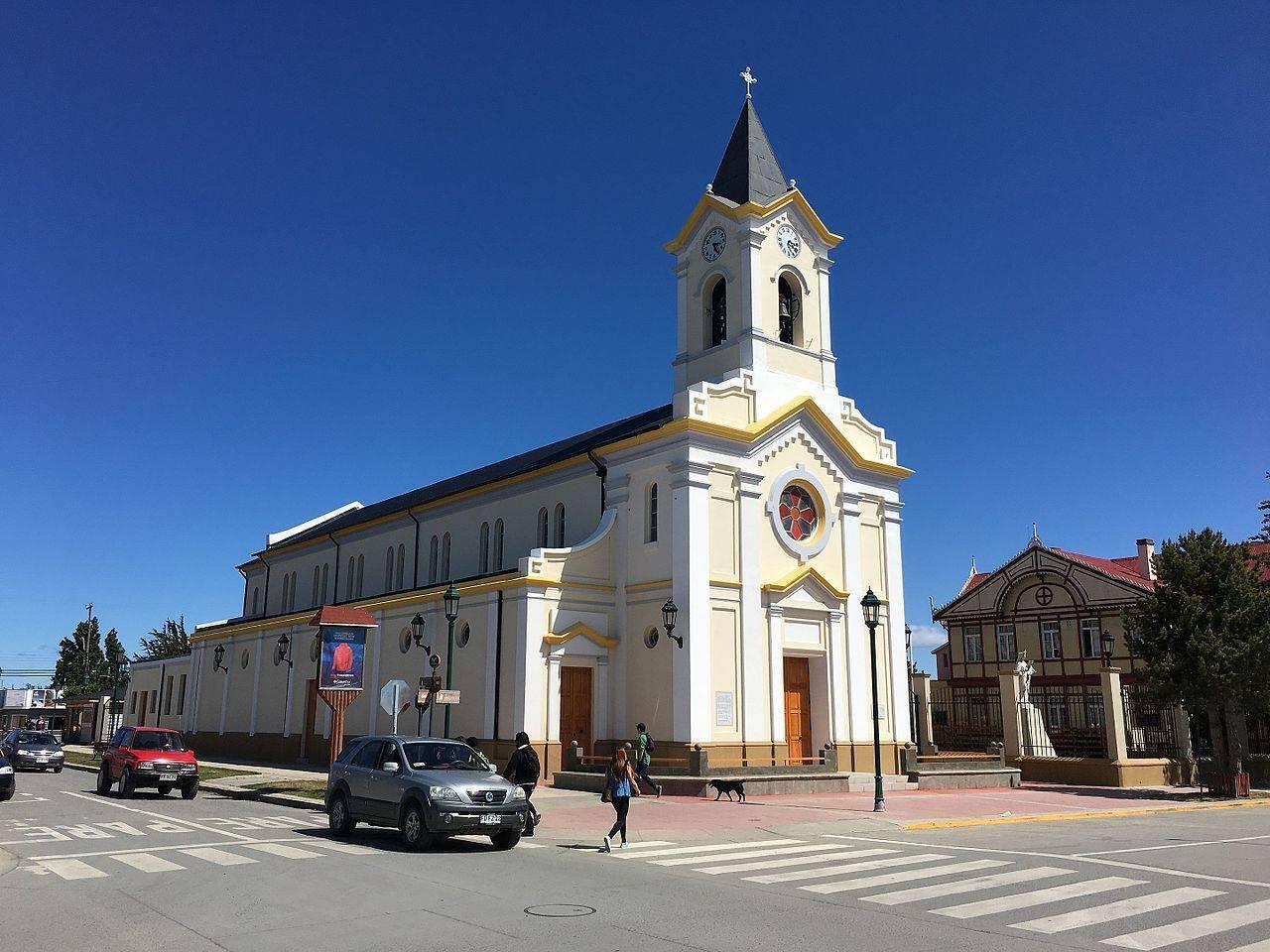 Église blanche avec clocher doré et croix, plaza pavée avec piétons et voitures, architecture coloniale sud-américaine