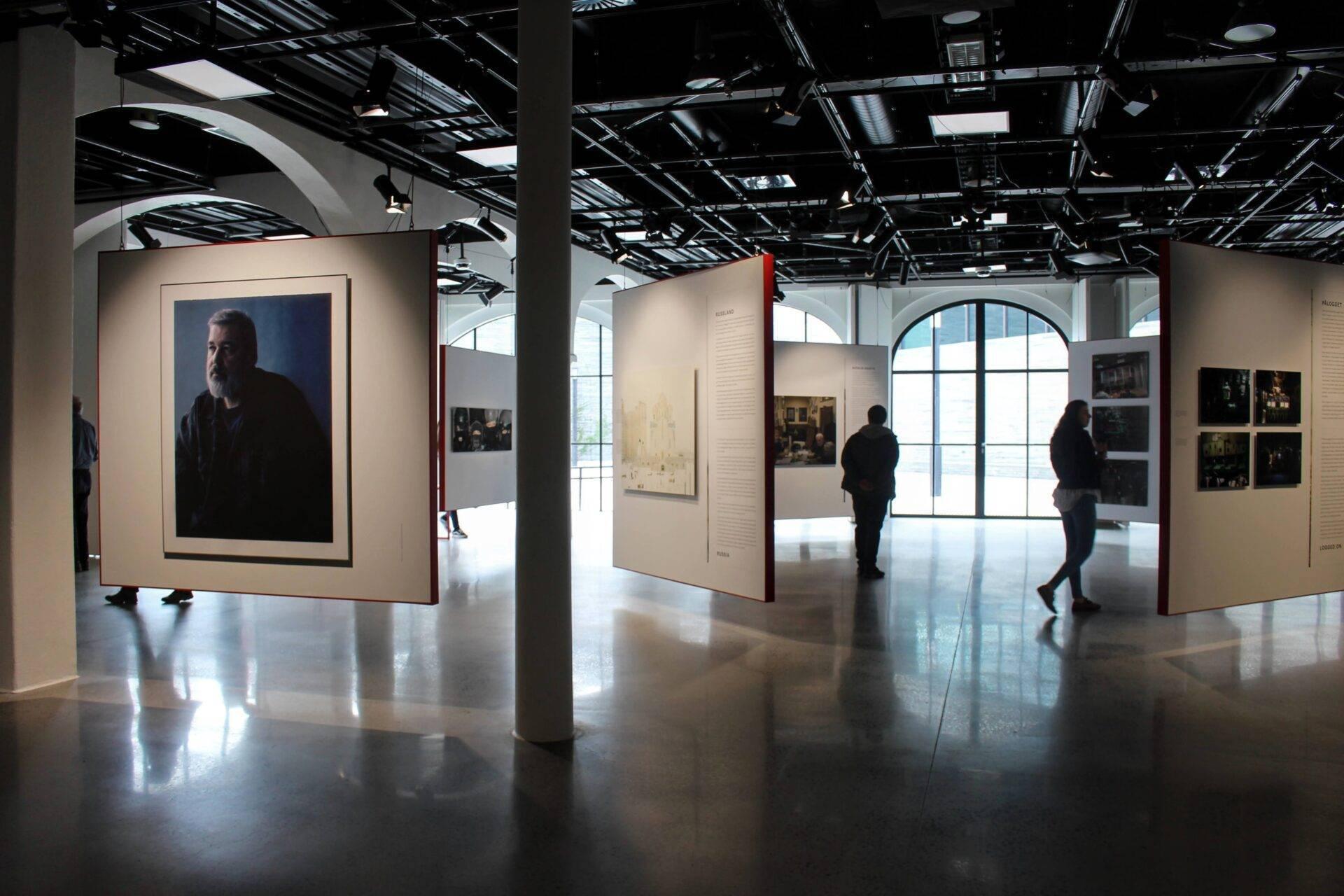 Intérieur d’une galerie d’art contemporain avec visiteurs admirant des portraits et installations photographiques sur panneaux blancs