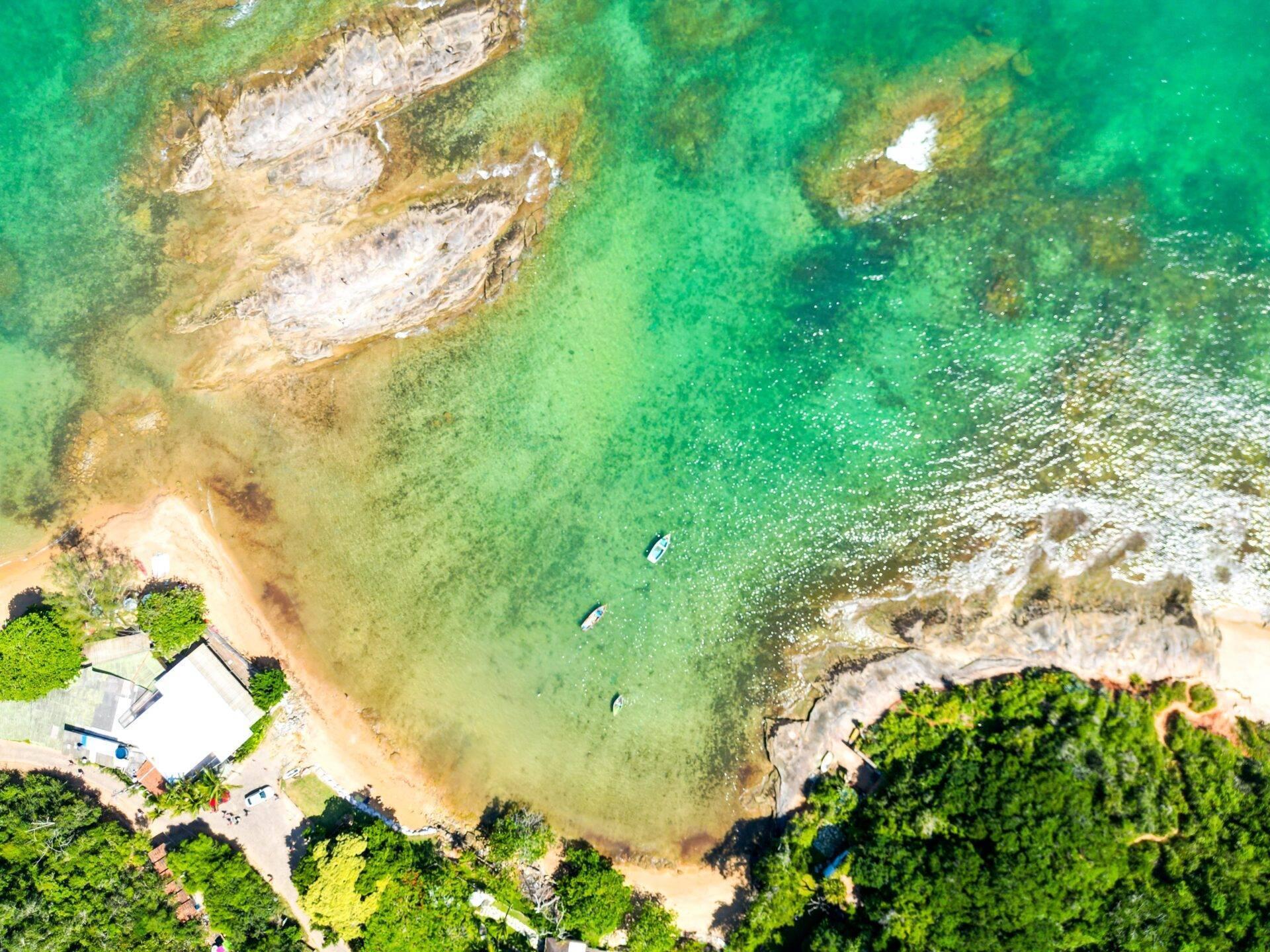 Vue aérienne d’une petite crique côtière avec plage de sable, eaux turquoise cristallines et formations rocheuses blanches