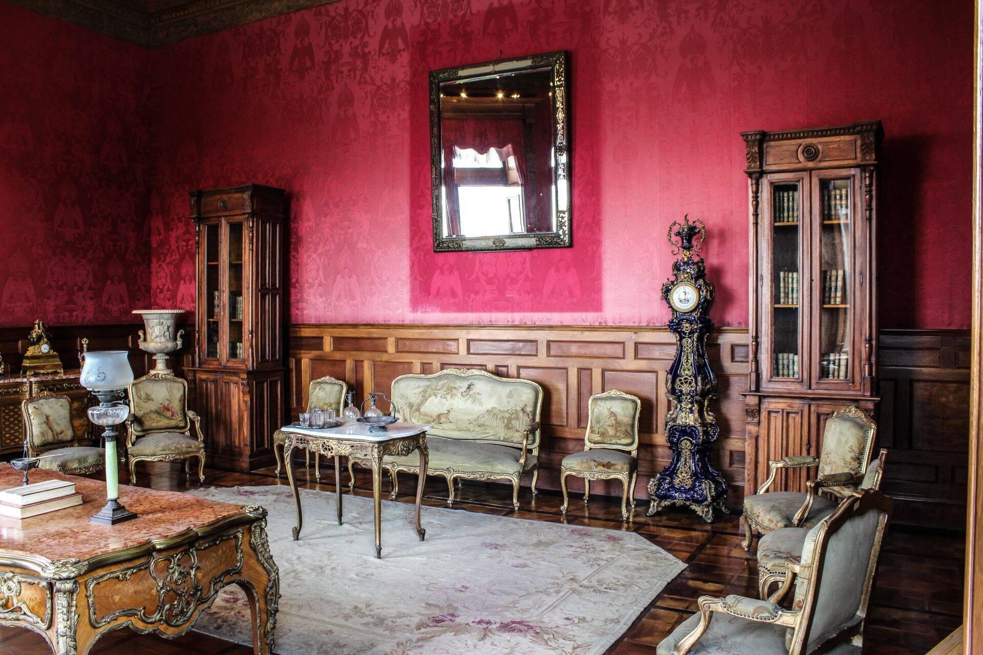 Un salon aristocratique aux murs rose fuchsia orné de mobilier doré et de boiseries, miroir et horloge décorée