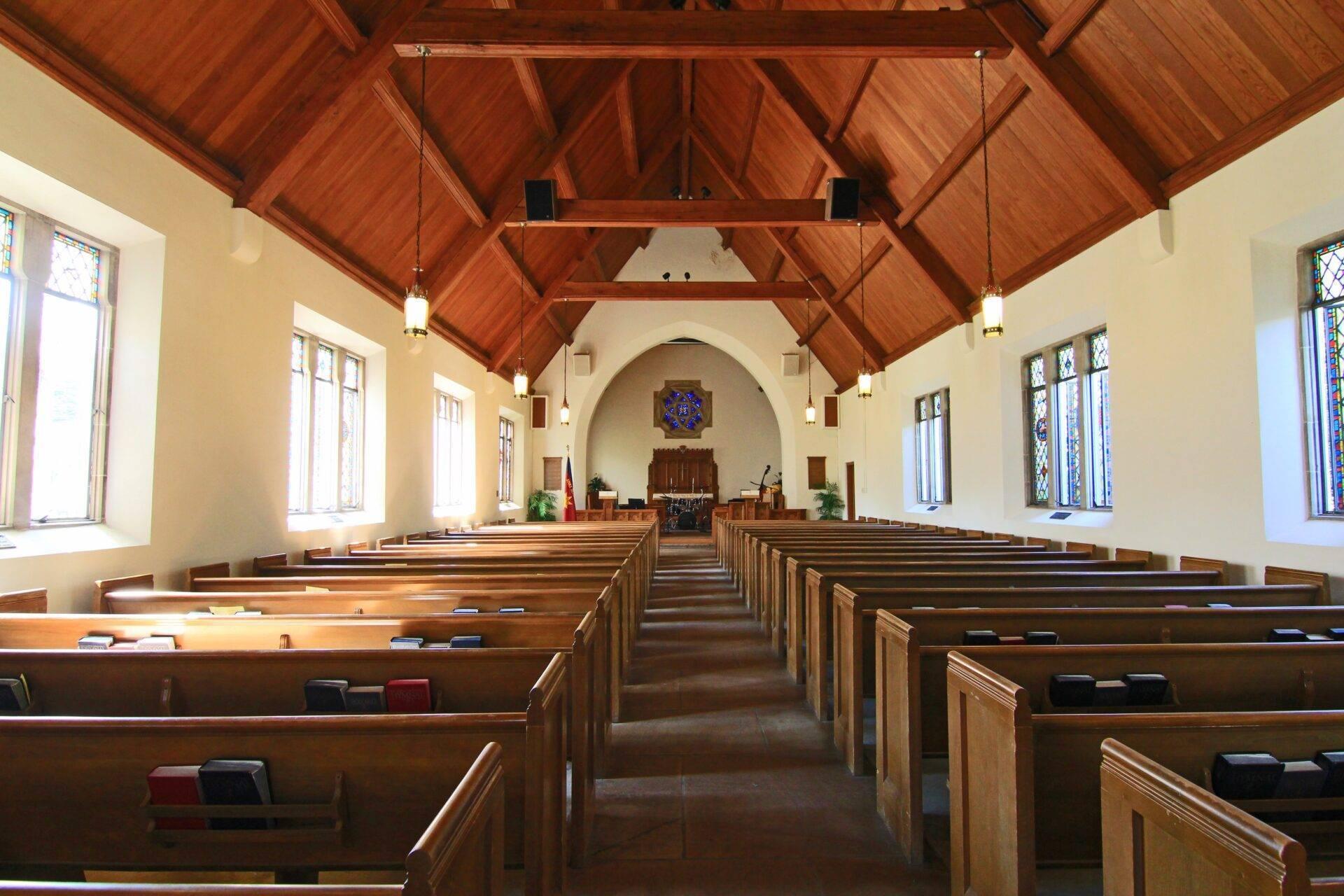 Intérieur d’une église avec bancs en bois, plafond en charpente apparente et vitraux colorés aux fenêtres