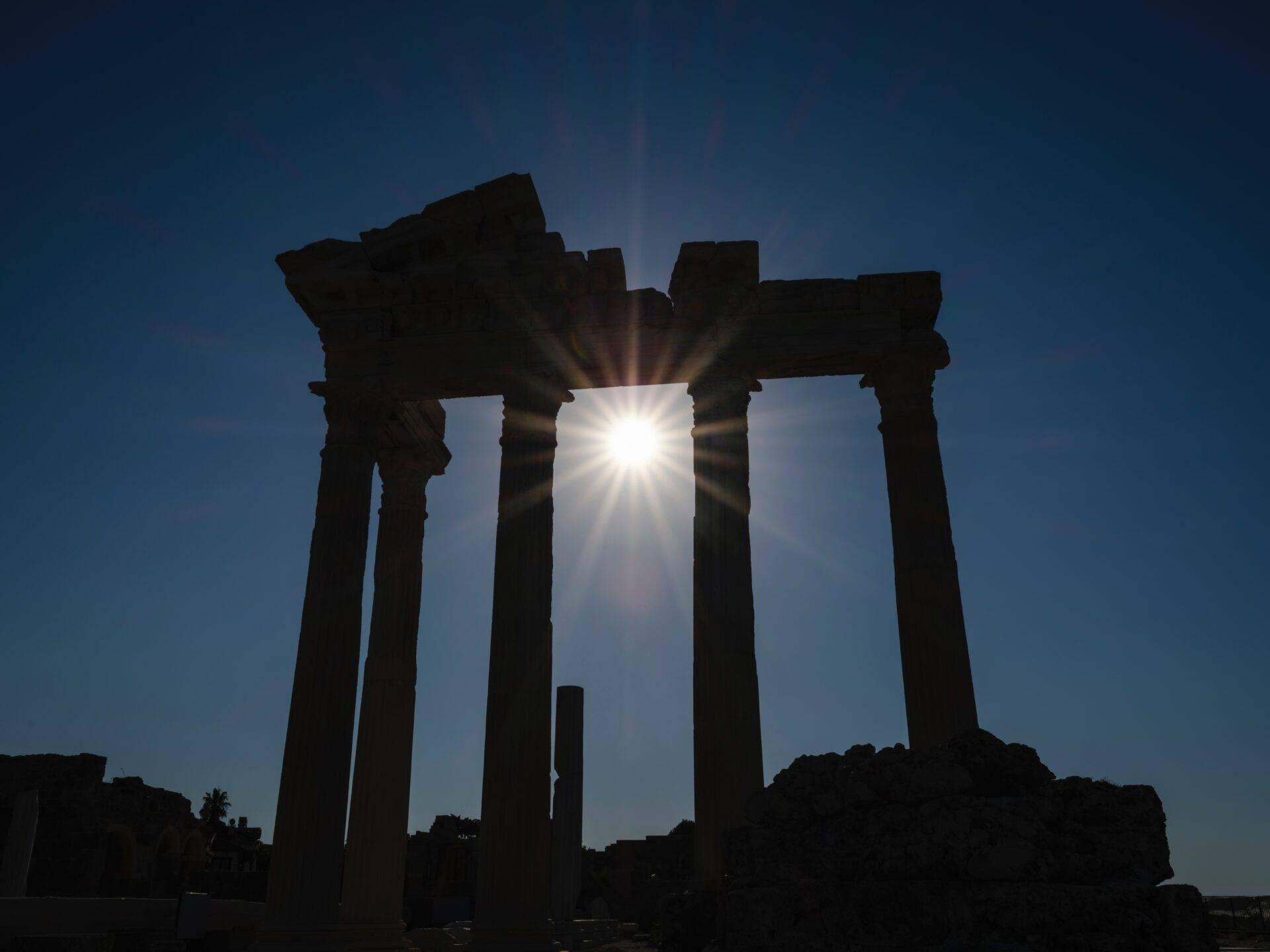 Silhouette de colonnes antiques contre le soleil éclatant sous un ciel bleu dégagé