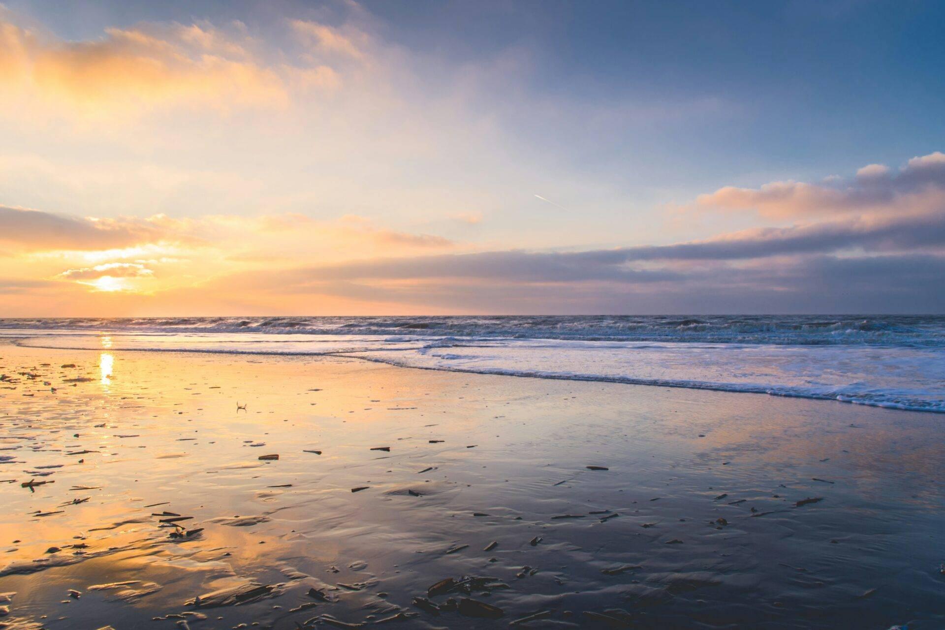 Coucher de soleil sur une plage de sable avec vagues et ciel doré aux teintes orangées