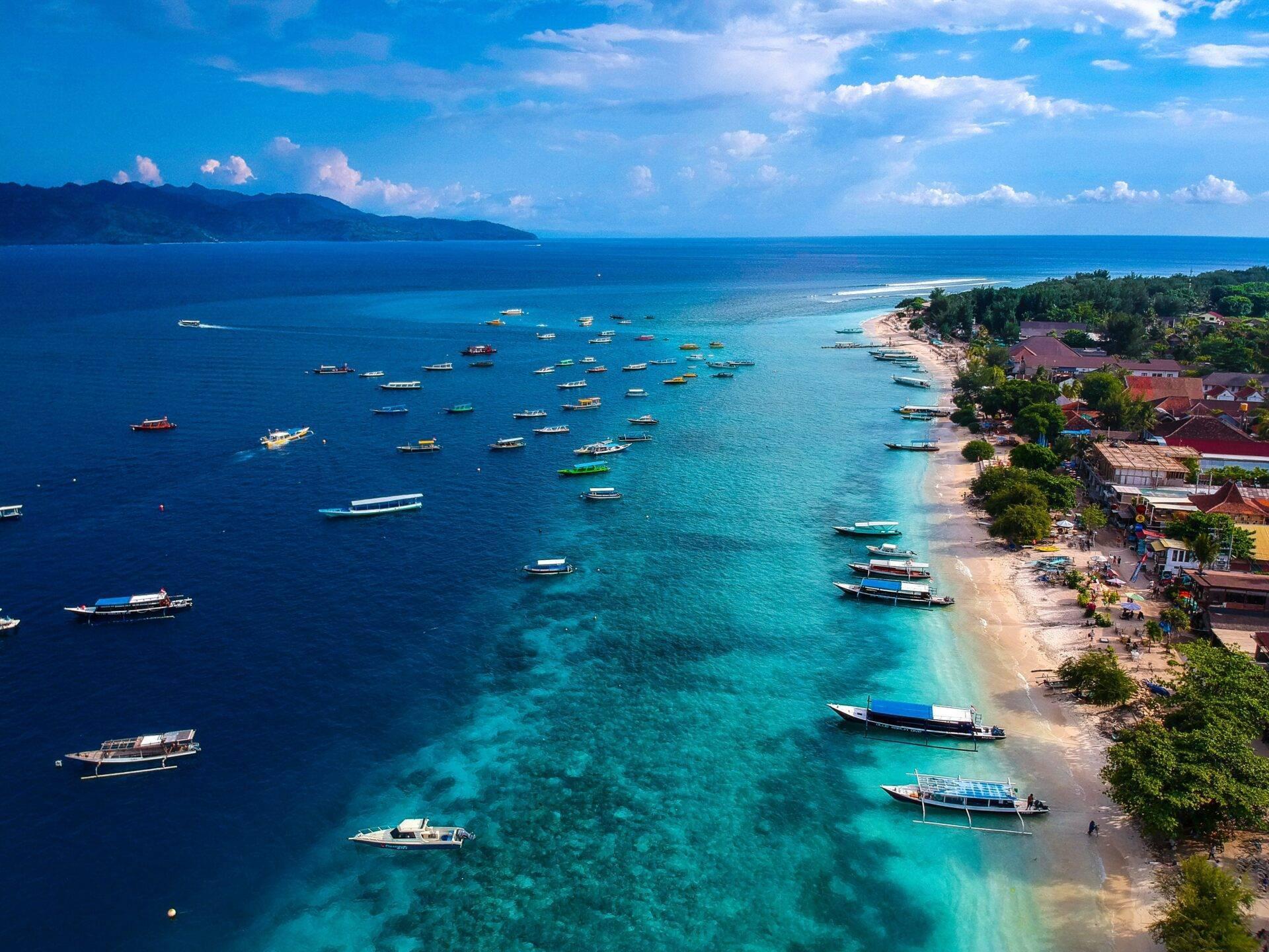 Vue aérienne d’une baie tropicale avec voiliers colorés ancrés près d’une plage de sable blanc bordée de maisons