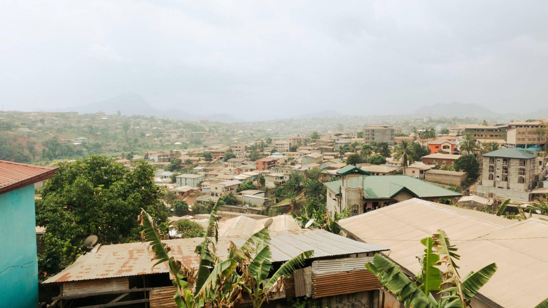 Vue panoramique d’une ville hillside avec maisons colorées, végétation tropicale et montagnes brumeuses en arrière-plan