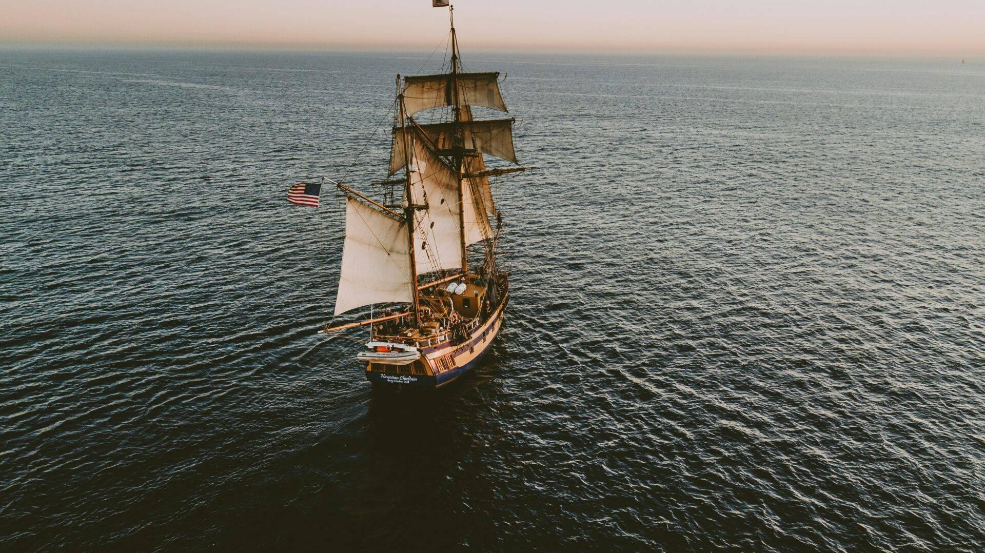 Un navire à voiles traditionnel américain navigue sur une mer calme au coucher du soleil