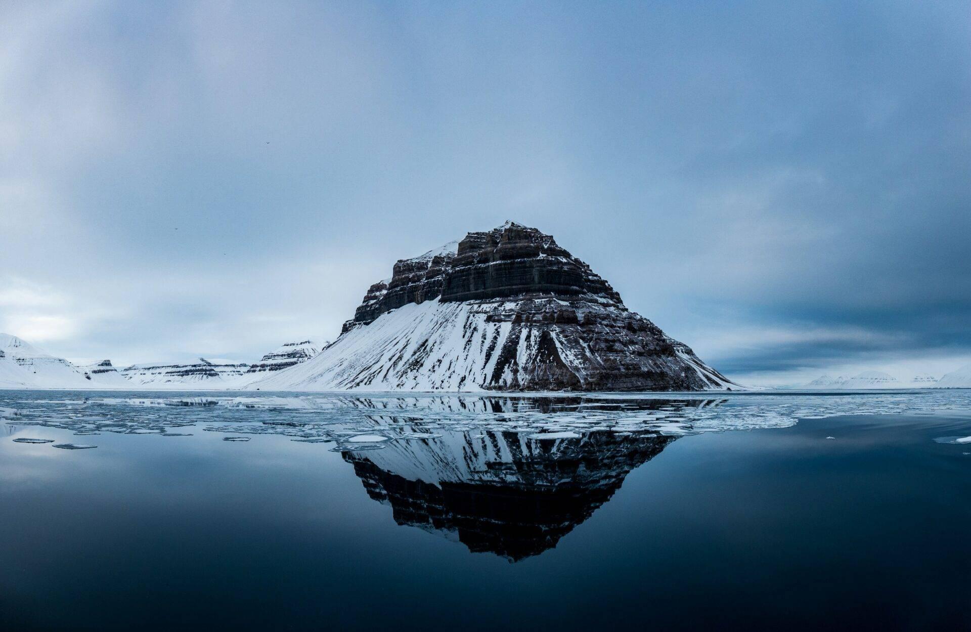Une montagne conique enneigée se reflète parfaitement dans une baie gelée aux eaux calmes, paysage arctique minimaliste