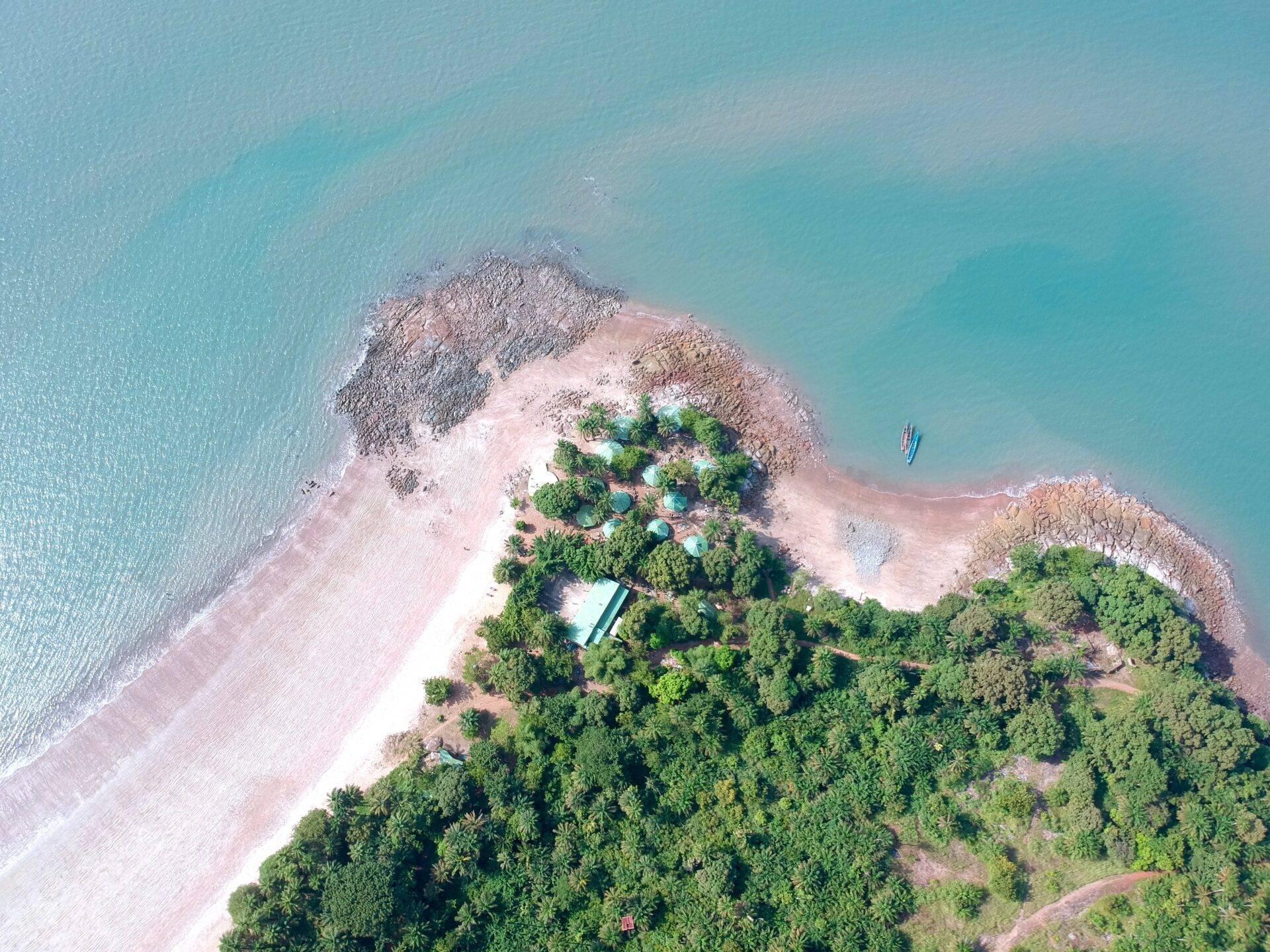 Vue aérienne d’une île côtière avec plage de sable blanc, forêt dense et eaux turquoise cristallines