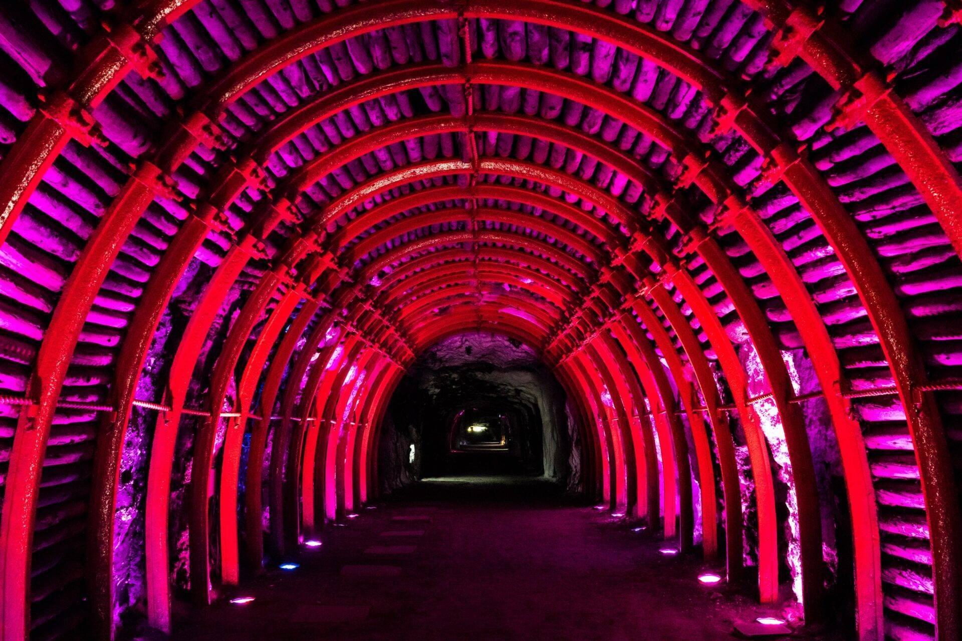 Un tunnel souterrain illuminé par des néons roses et rouges avec des arches métalliques successives