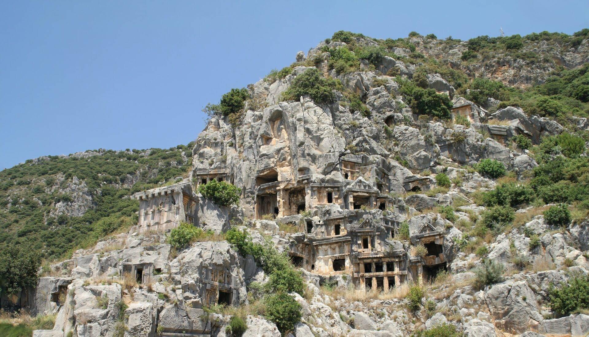 Tombes rupestres anciennes creusées dans une falaise rocheuse sous un ciel bleu dégagé
