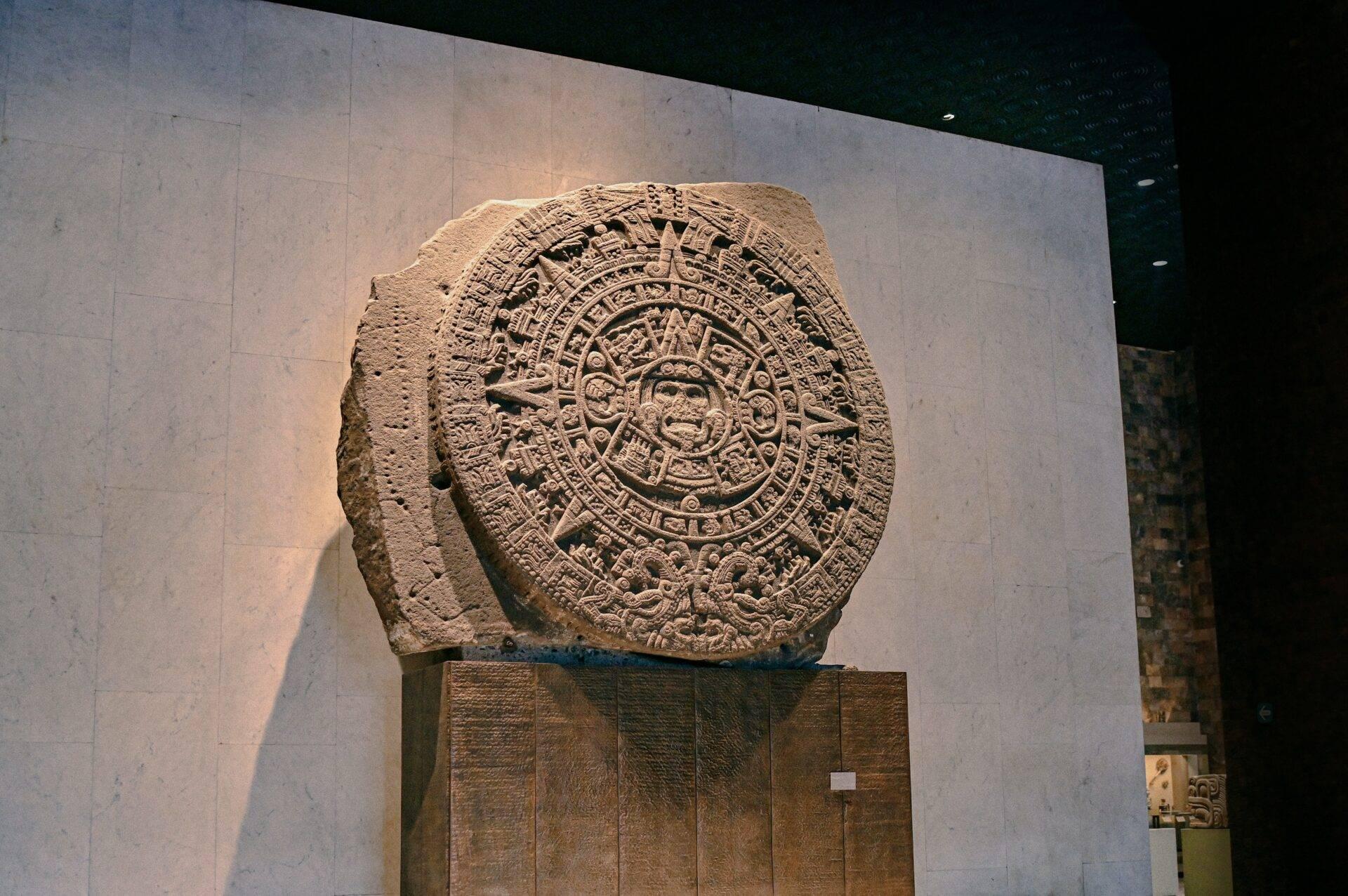 Pierre calendrier aztèque sculptée exposée dans un musée avec éclairage directionnel mettant en évidence les détails gravés