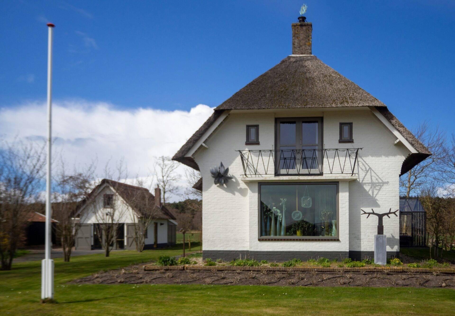 Une maison blanche traditionnelle aux Pays-Bas avec toit de chaume pointu et balcon en fer forgé