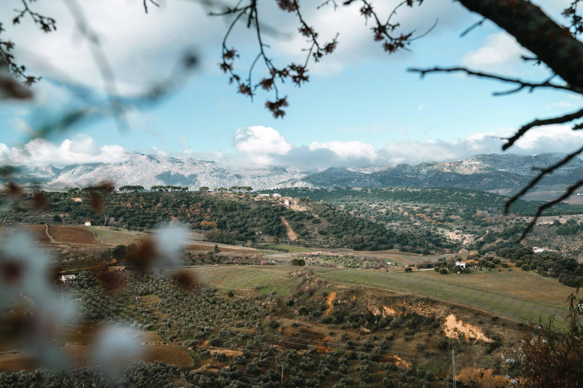 Vue panoramique sur une vallée méditerranéenne avec montagnes enneigées, villages dispersés et champs cultivés sous ciel bleu