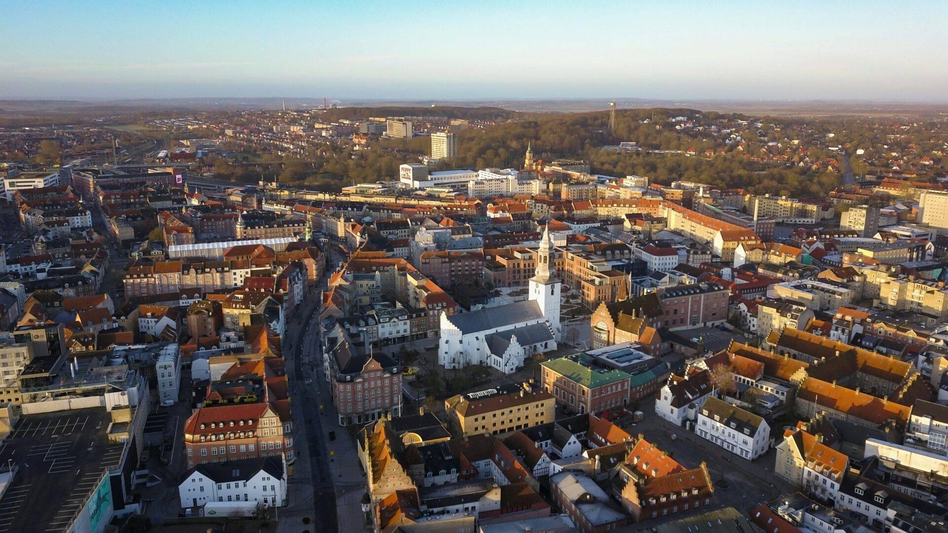 Vue aérienne d’une ville européenne avec églises, toits orangés et espaces verts en arrière-plan