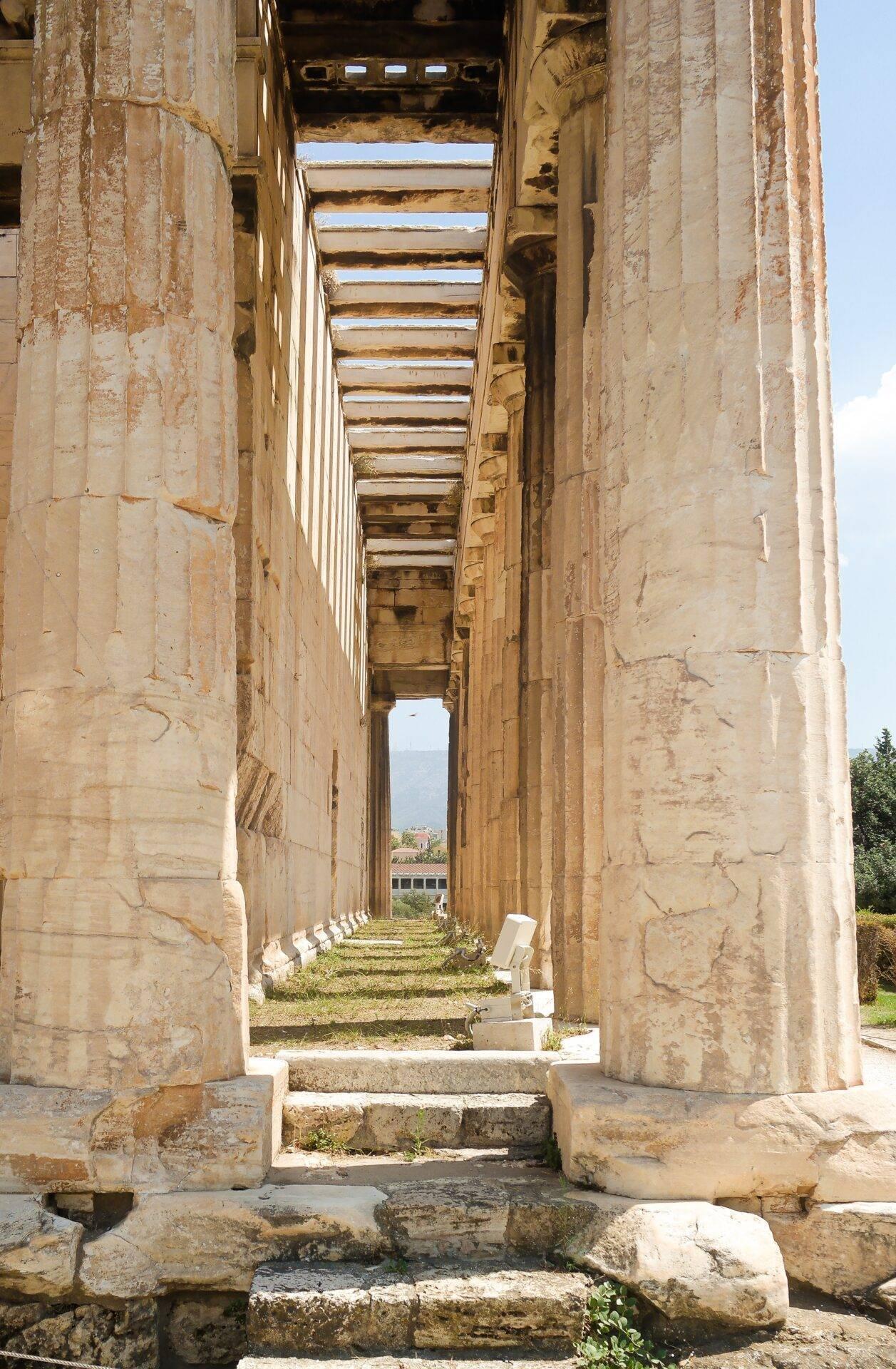 Couloir de colonnes antiques en pierre calcaire créant une perspective enfilée vers un paysage montagneux lointain