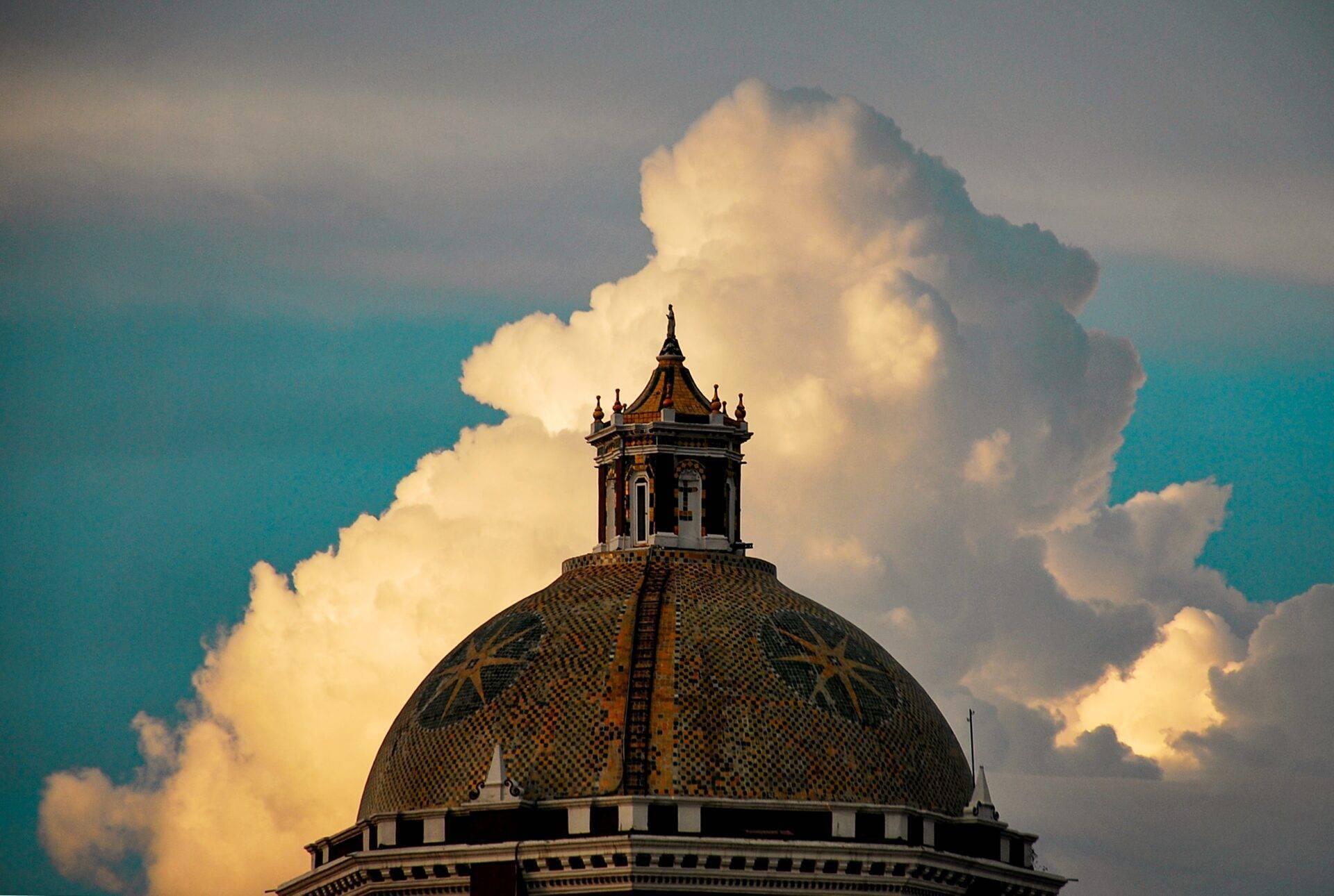 Un dôme jaune et noir de style colonial mexicain surmonté d’une lanterne, sous un ciel turquoise avec nuages blancs