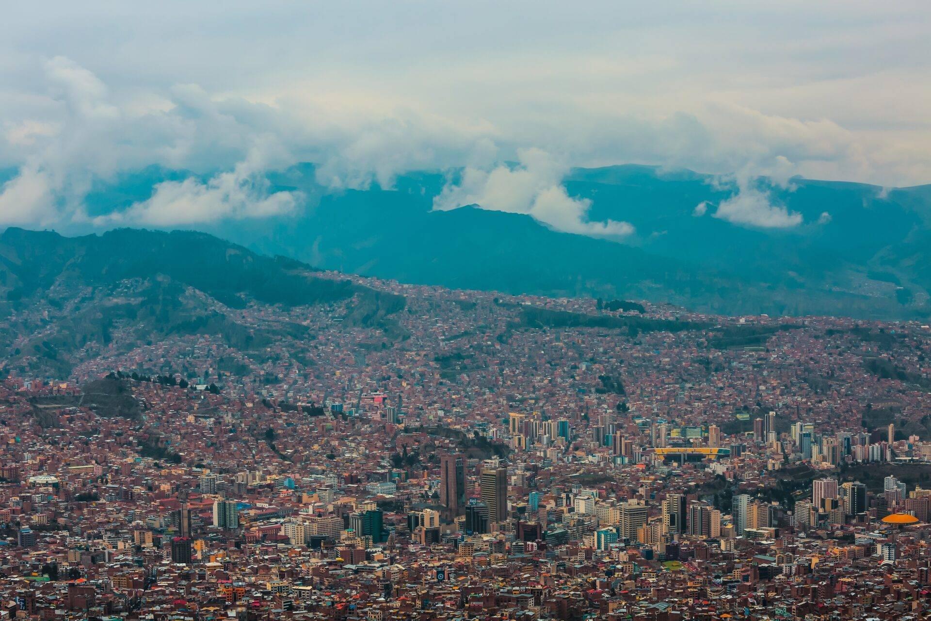 Vue aérienne d’une grande ville andine densément construite, encadrée par des montagnes verdoyantes sous un ciel nuageux