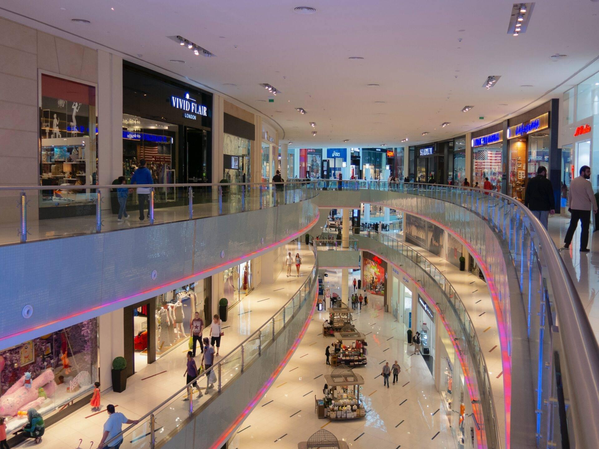 Intérieur d’un centre commercial moderne avec plusieurs étages, boutiques illuminées et allées commerçantes animées