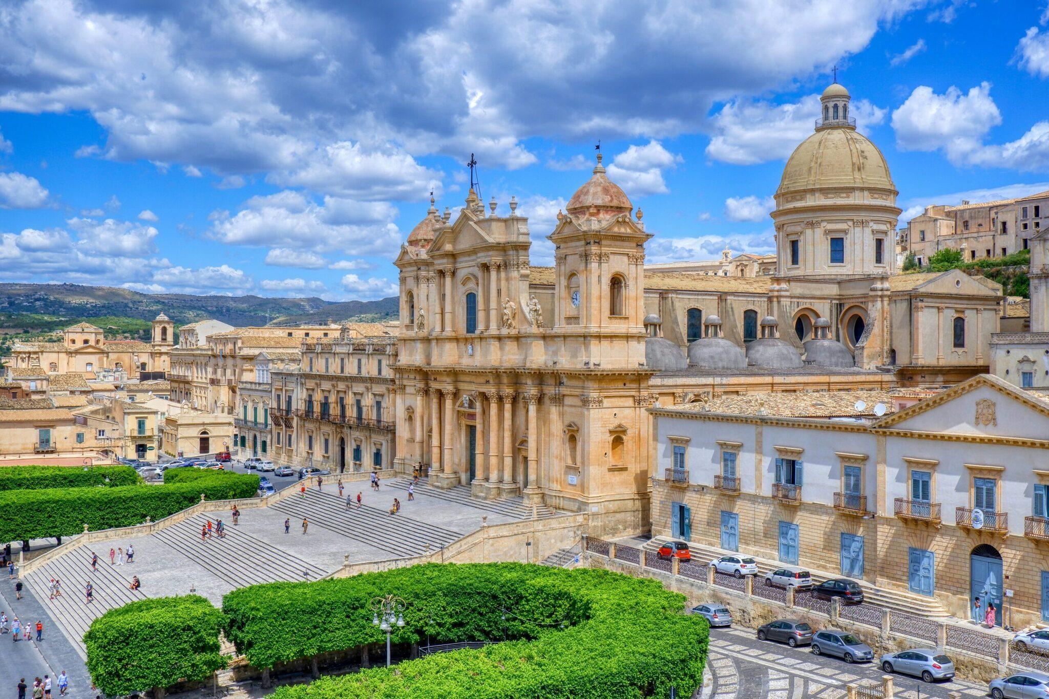Une magnifique cathédrale baroque avec dôme doré domine une piazza pavée dans une ville sicilienne historique sous ciel bleu