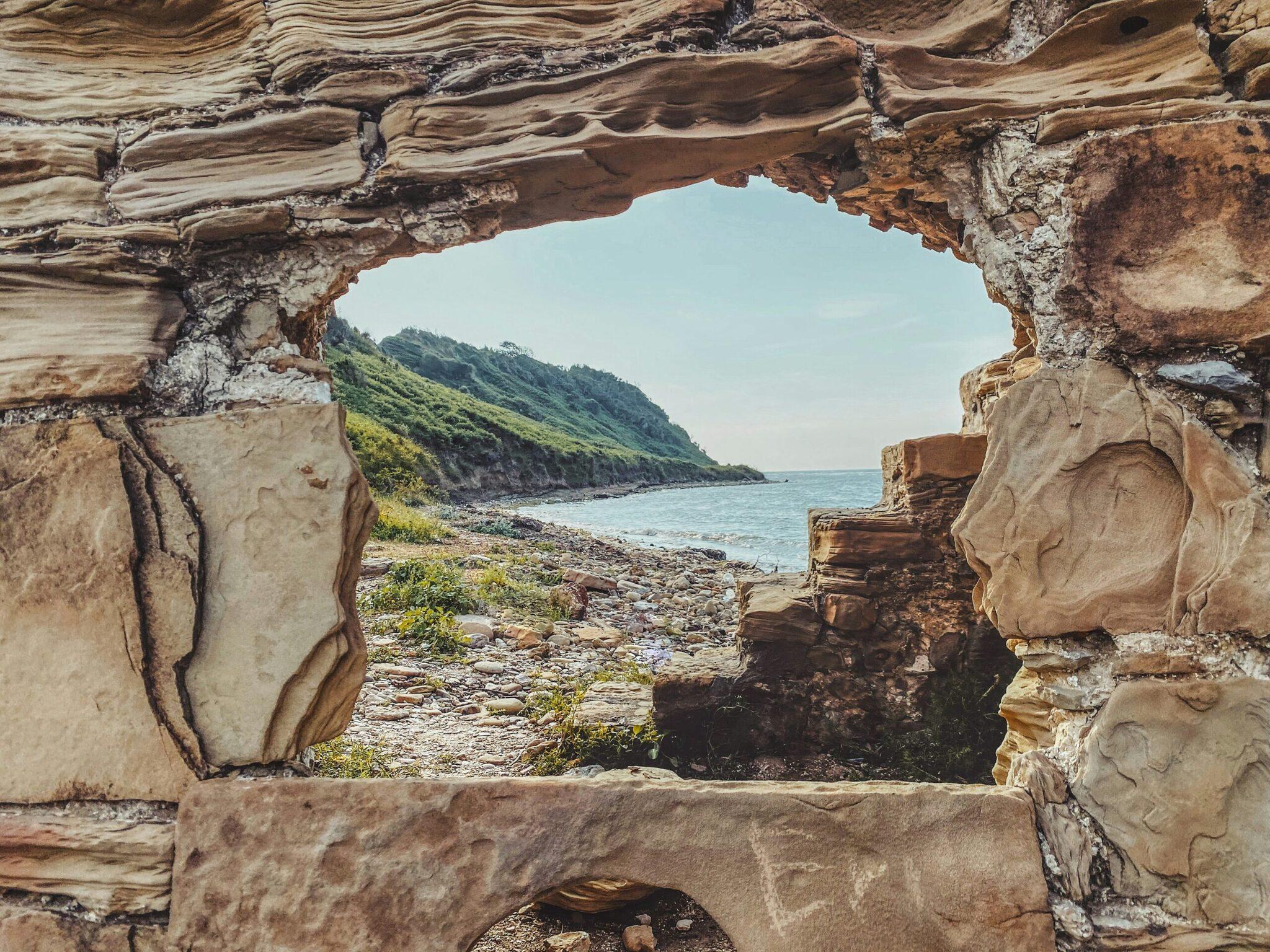 Vue à travers des ruines de pierre sur une baie côtière avec falaise verdoyante et mer turquoise